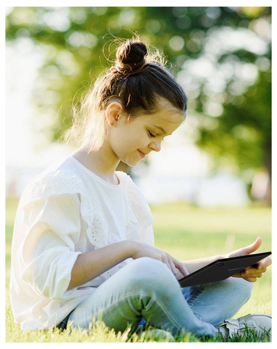 Une jeune fille est assise sur l'herbe dans un parc, concentrée sur une tablette. Elle sourit légèrement, la lumière du soleil filtrant à travers les arbres en arrière-plan.