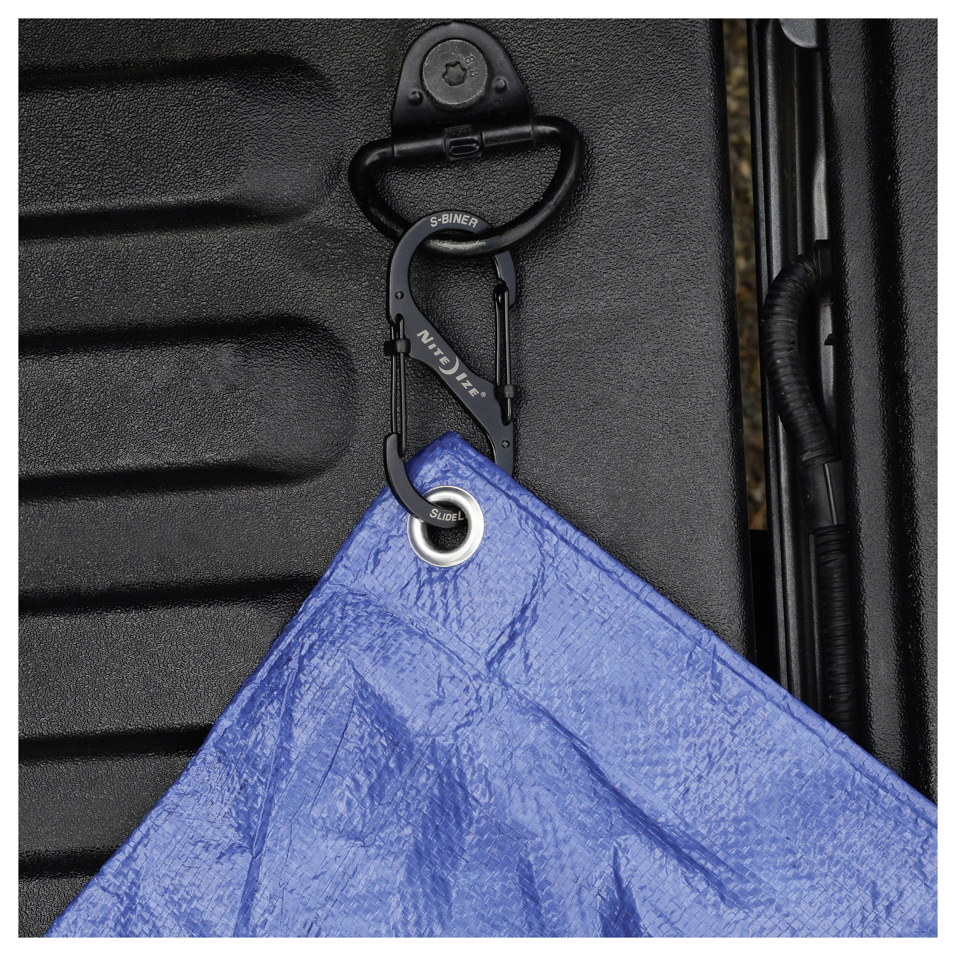 Une bâche bleue fixée avec un mousqueton noir sur une surface texturée ; utilisée pour couvrir ou protéger des objets.