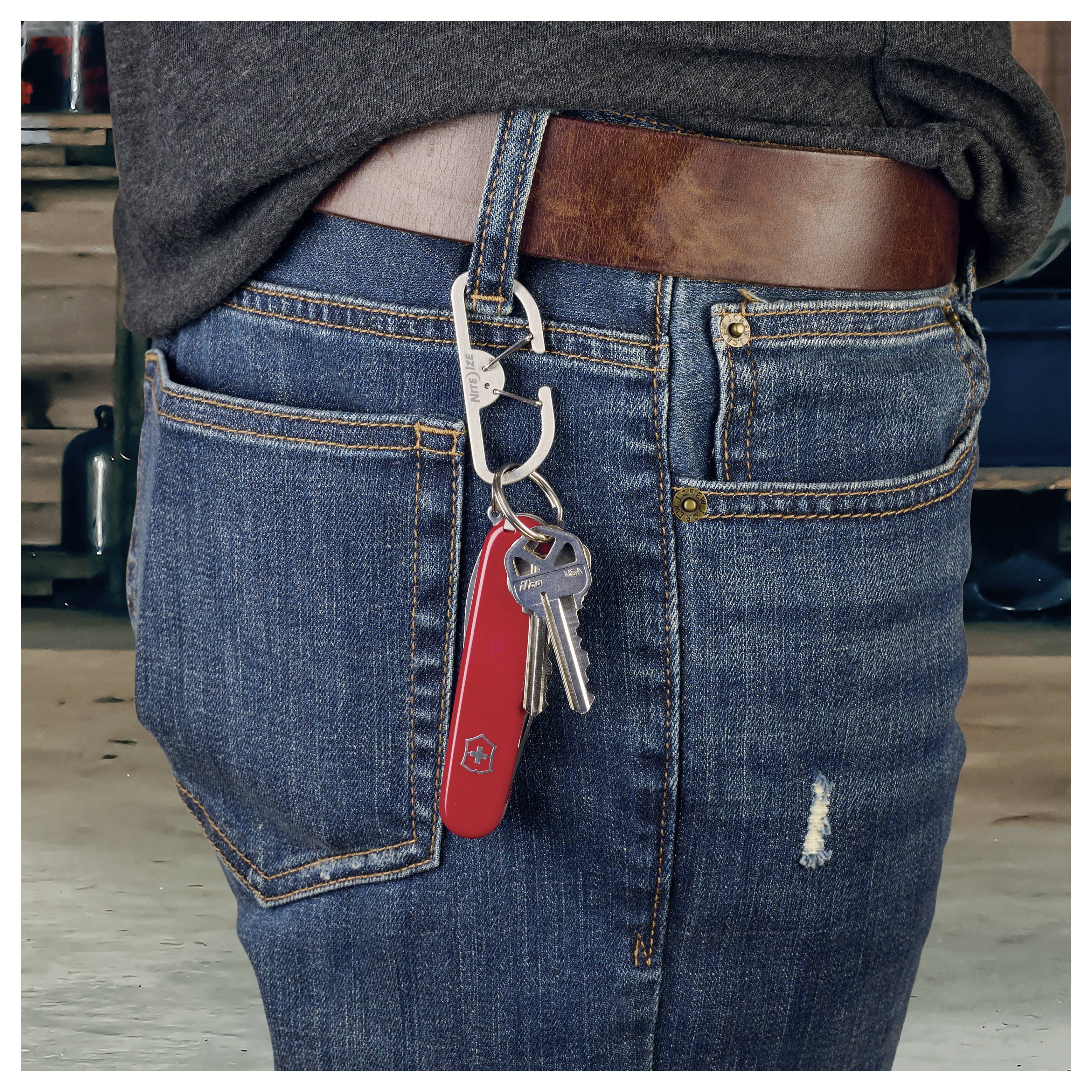 Une personne portant un jean, avec des clés et un couteau suisse rouge sur un porte-clés accroché à une passant de ceinture, sur un fond industriel.
