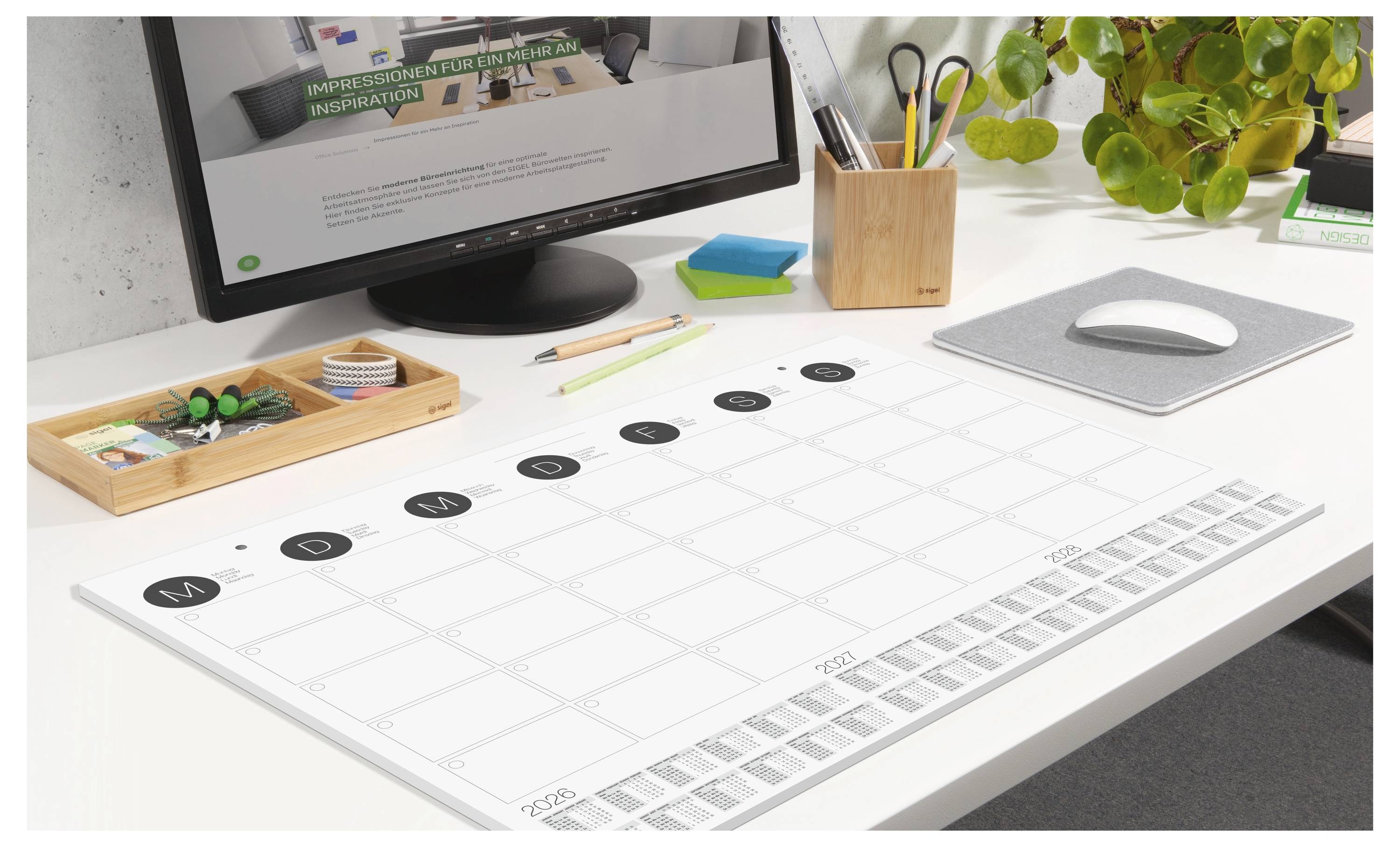 Un espace de travail bien rangé avec un agenda-calendrier sur le bureau, entouré de papeterie, d'une plante et d'un ordinateur affichant une page web.