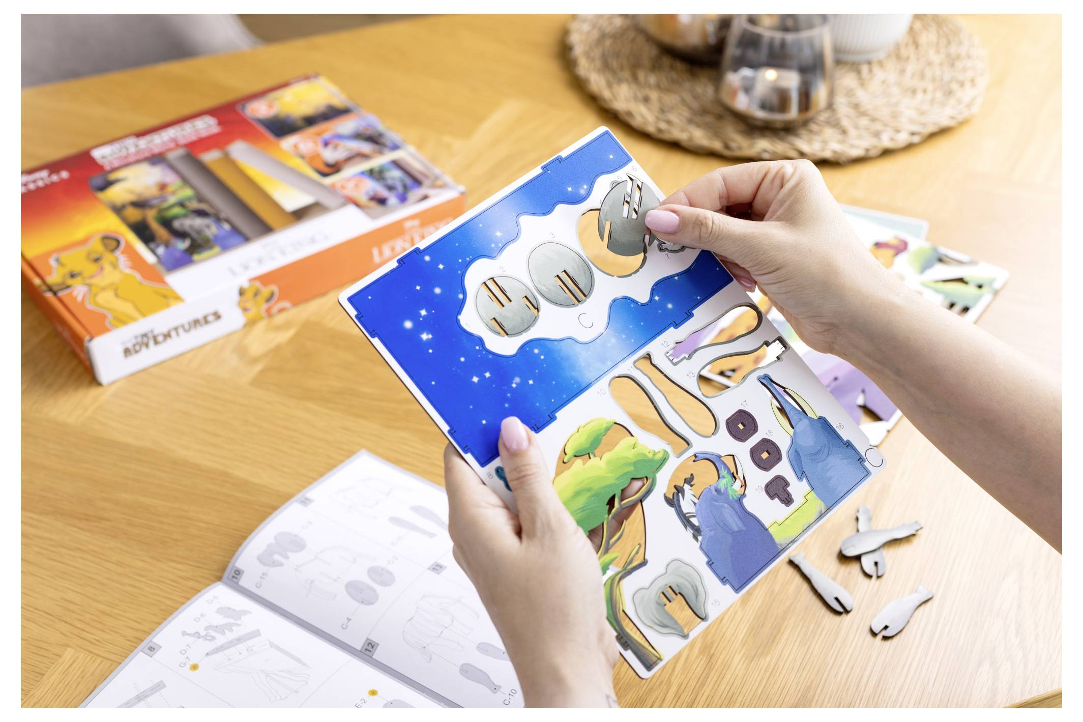 Une personne tient une feuille découpée colorée d'un jeu de puzzle pour enfants sur une table en bois, avec d'autres pièces de puzzle et des instructions à proximité.