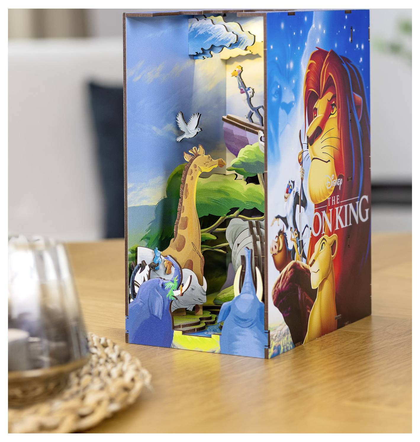 Une scène en pop-up 3D du 'Roi Lion' présentant des personnages animés tels qu'un lion et des girafes sur un fond coloré et dynamique.