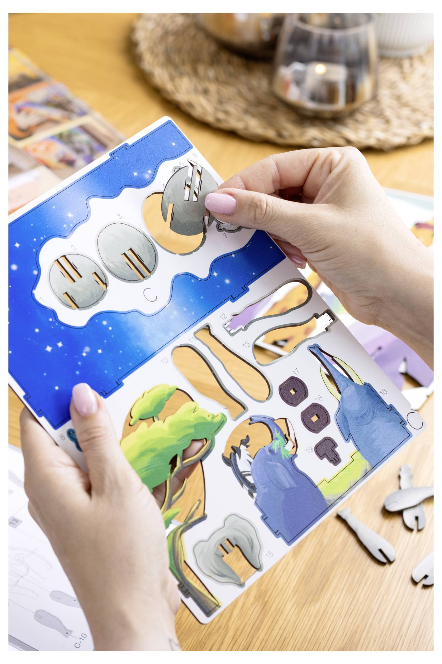 Une personne assemble un puzzle 3D coloré sur le thème de la nature et de l'espace. Les pièces représentent des arbres, le ciel et des planètes. Des mains tiennent le puzzle.