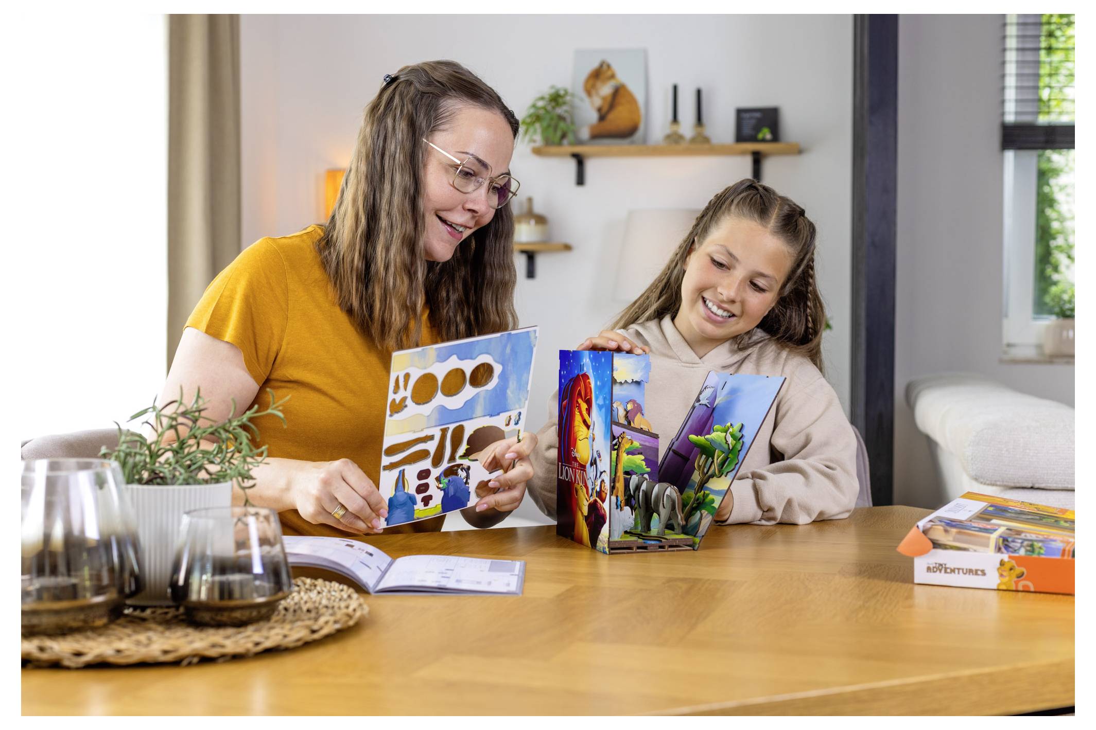Une femme et une jeune fille sont assises à une table, absorbées dans la lecture de livres richement illustrés, souriantes. Un salon douillet se trouve en arrière-plan.