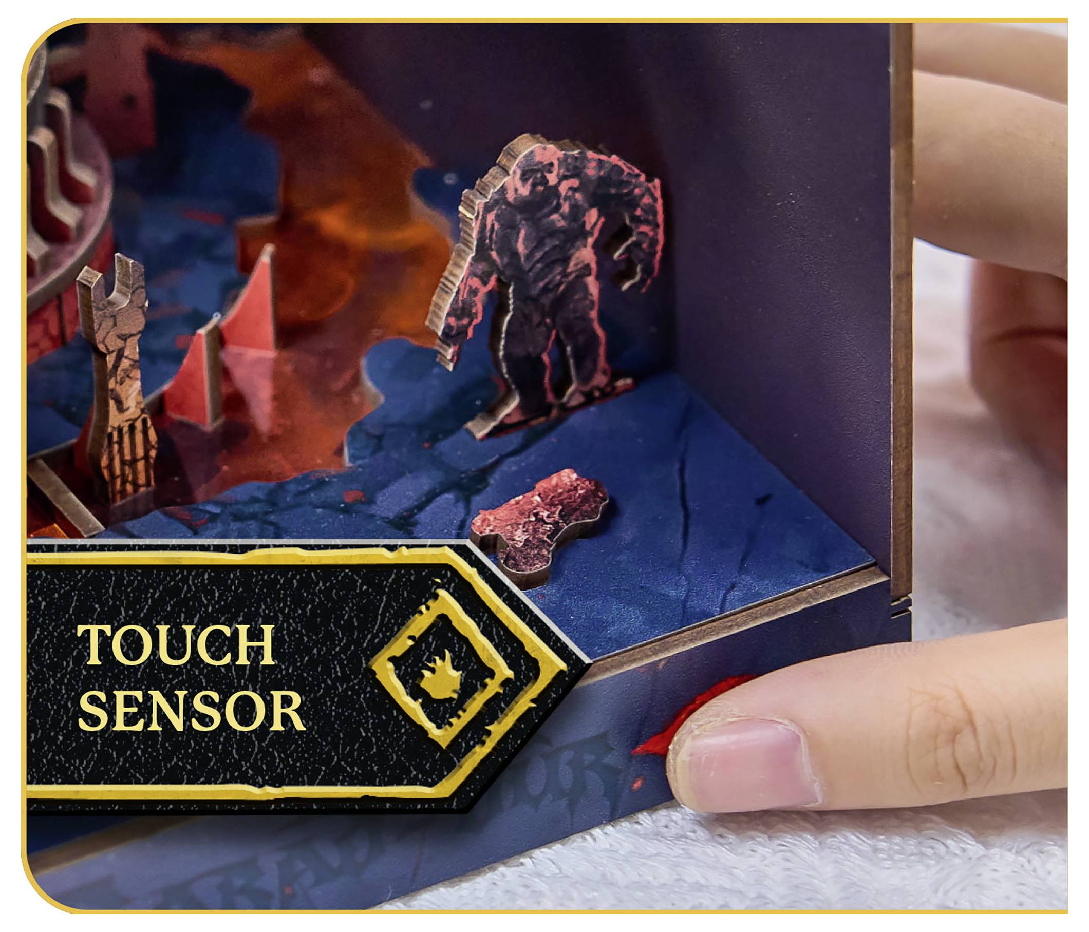Une personne interagit avec un jeu de société, en activant une zone de 'CAPTEUR TACTILE' qui libère une figurine sur une surface colorée et texturée.