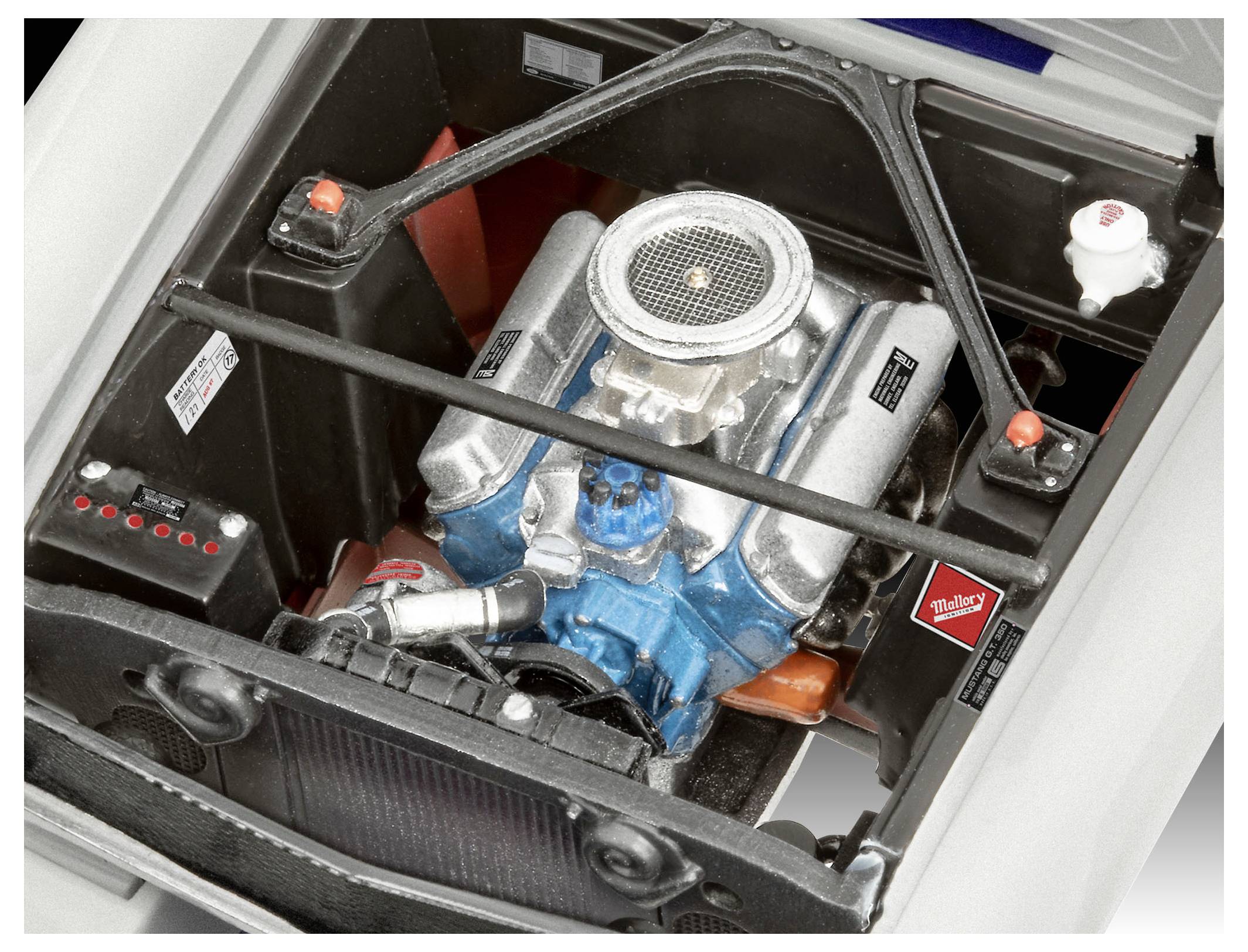 Vue rapprochée d'un moteur de voiture recouvert de divers composants argentés et bleus, entouré de supports métalliques et de petites étiquettes.