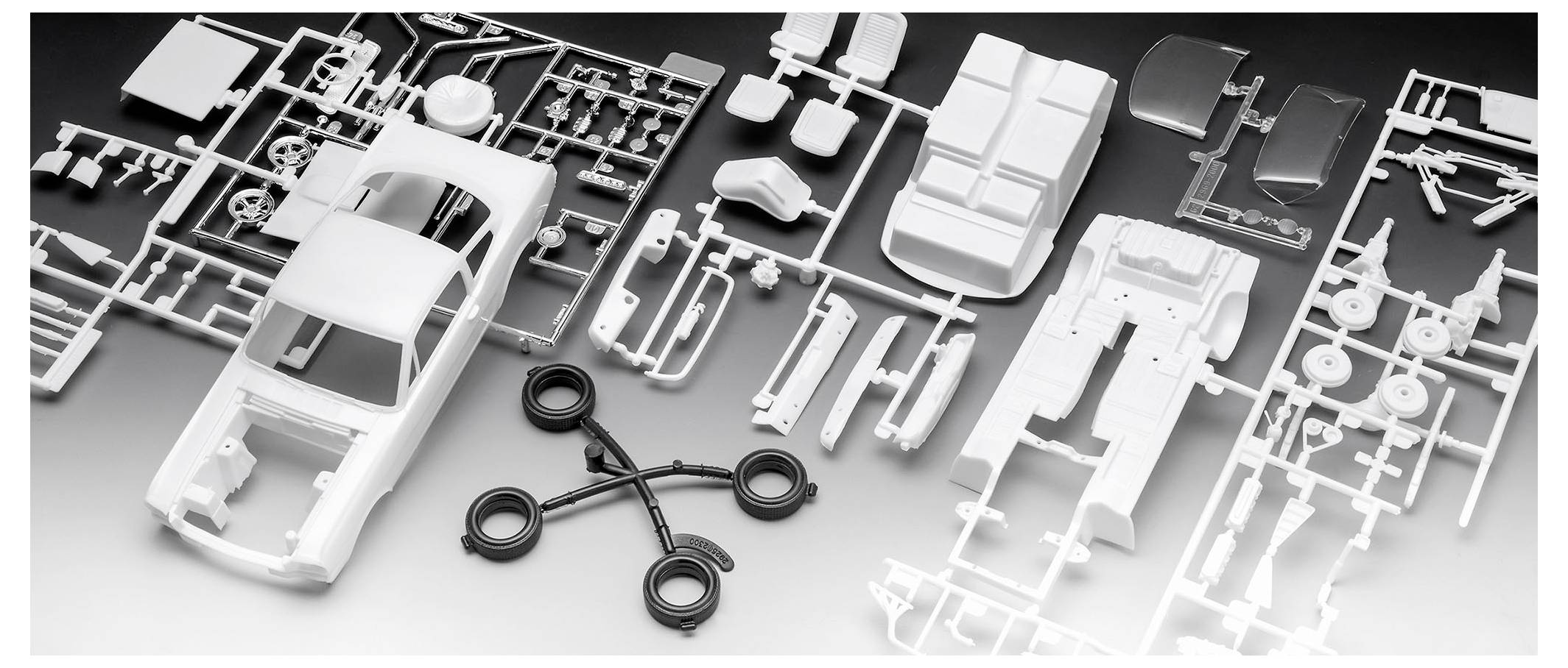 Kit de maquette de voiture avec des pièces en plastique démontées comprenant une carrosserie, des roues et des composants d'intérieur, disposés sur une surface plane.