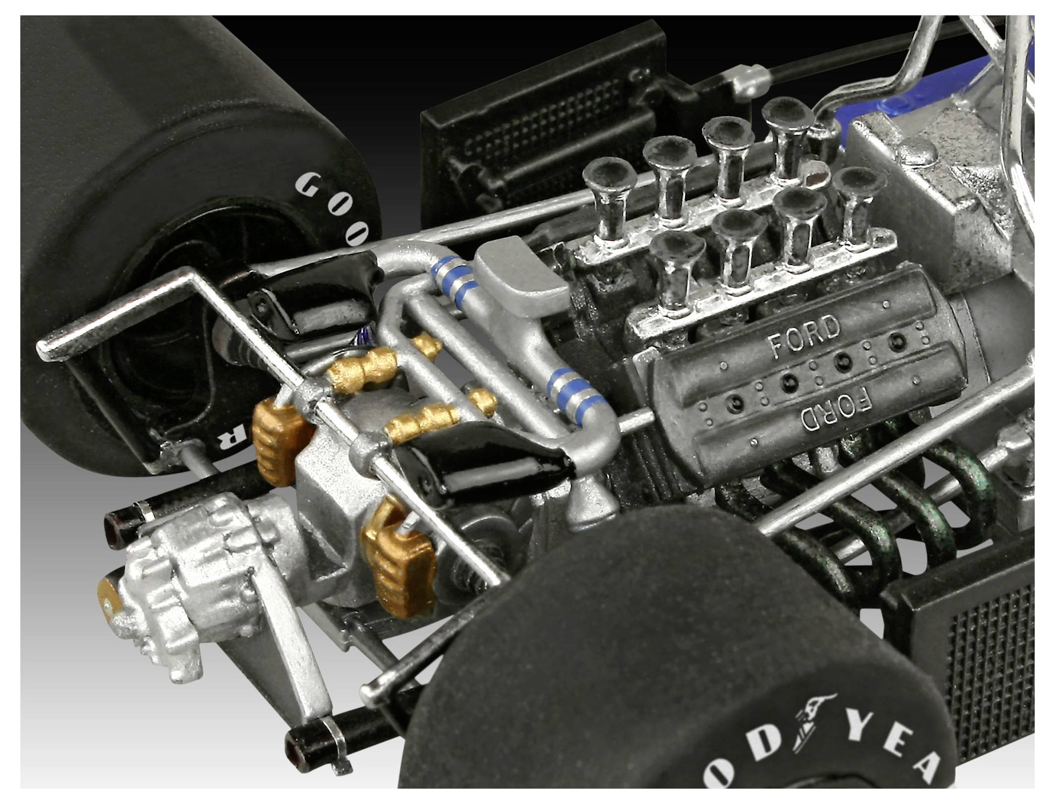Gros plan sur le moteur d'une voiture de course miniature avec marquage 'Ford' visible, pneus Goodyear et détails métalliques et tubulaires complexes.