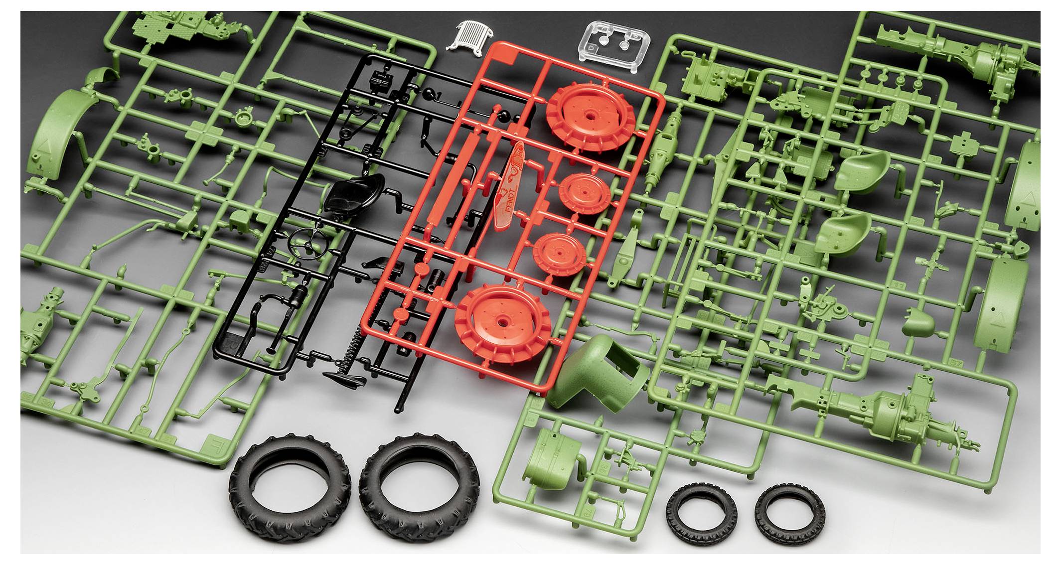 Pièces de maquette en plastique d'un tracteur, dispersées sur une surface, comprenant des roues, des essieux et des composants de carrosserie en vert, rouge et noir.