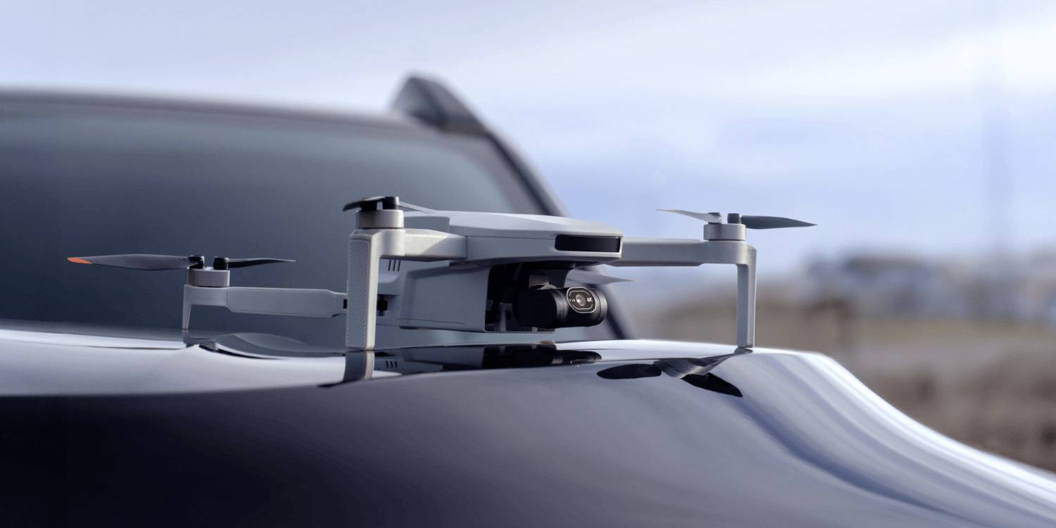 Un drone est posé sur le capot d'une voiture élégante dans un décor extérieur flou, évoquant des thèmes de technologie avancée ou de transport.