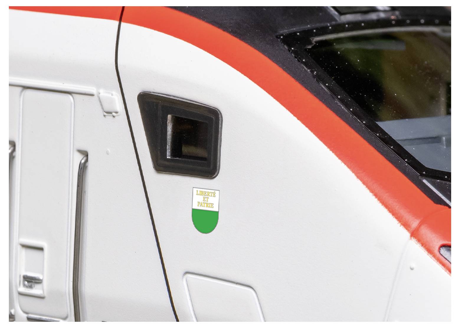 Un gros plan d'une porte de train avec un extérieur rouge et blanc, présentant un petit écusson italien qui porte l'inscription « Liguria di Ponente ».