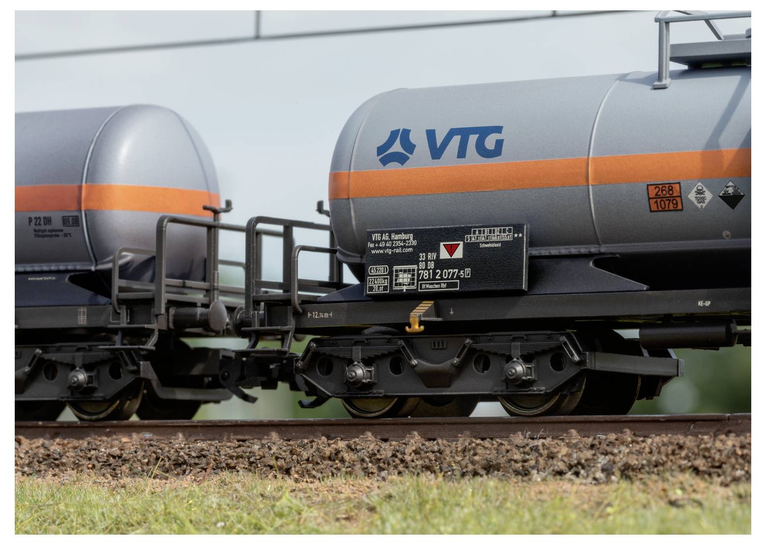 Deux wagons-citernes ferroviaires gris avec des bandes oranges et le logo « VTG », positionnés sur des voies ferrées dans un environnement extérieur.