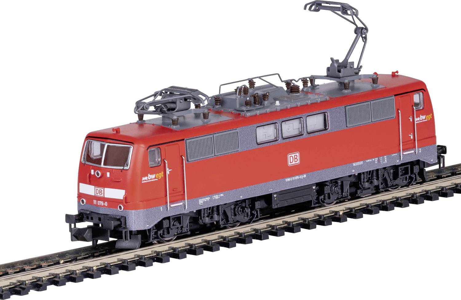 Un petit modèle d'une locomotive électrique rouge, marquée des logos 'DB', circulant sur un rail avec des connexions électriques aériennes.