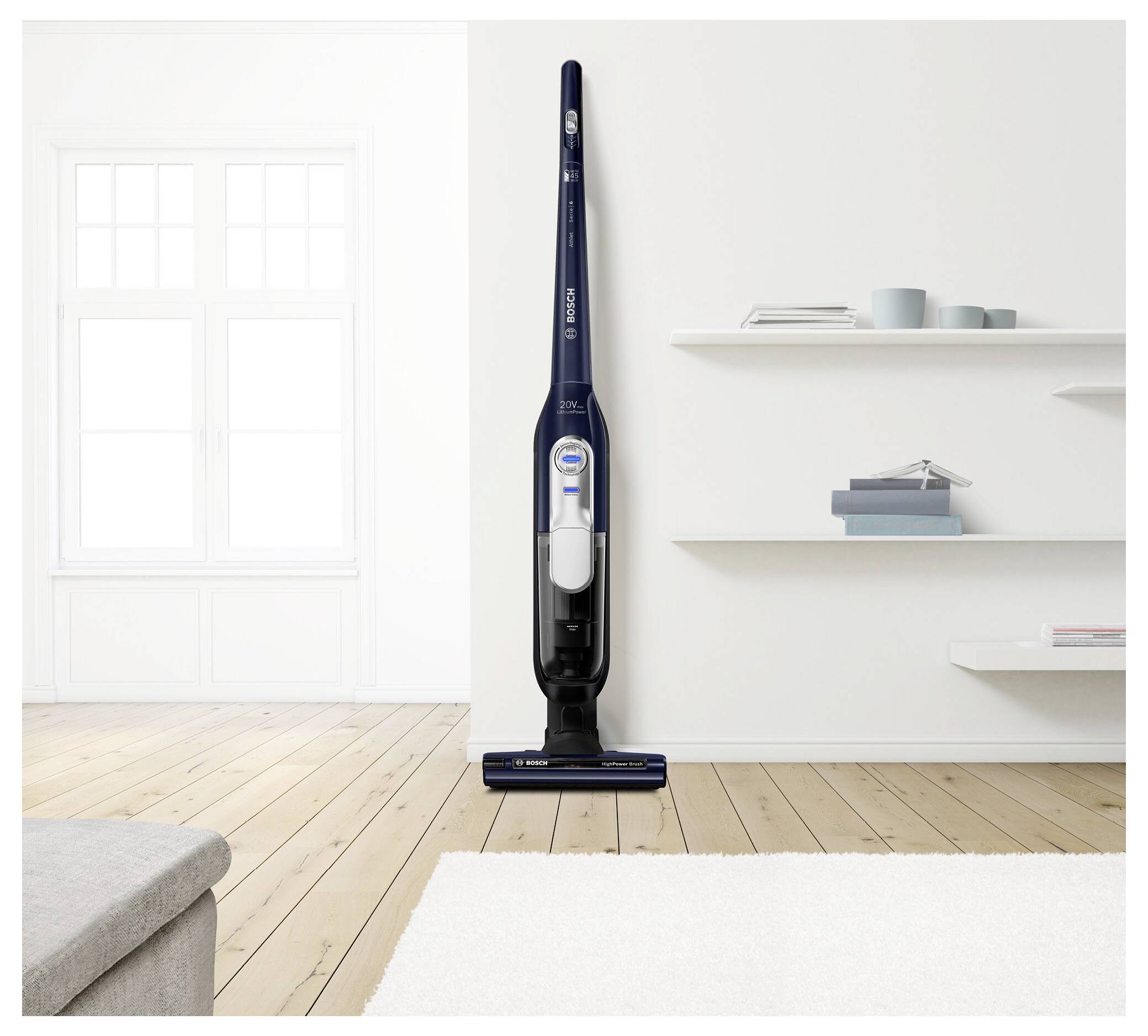 Un aspirateur sans fil est debout sur un parquet dans un salon moderne et minimaliste aux murs blancs et avec un tapis.