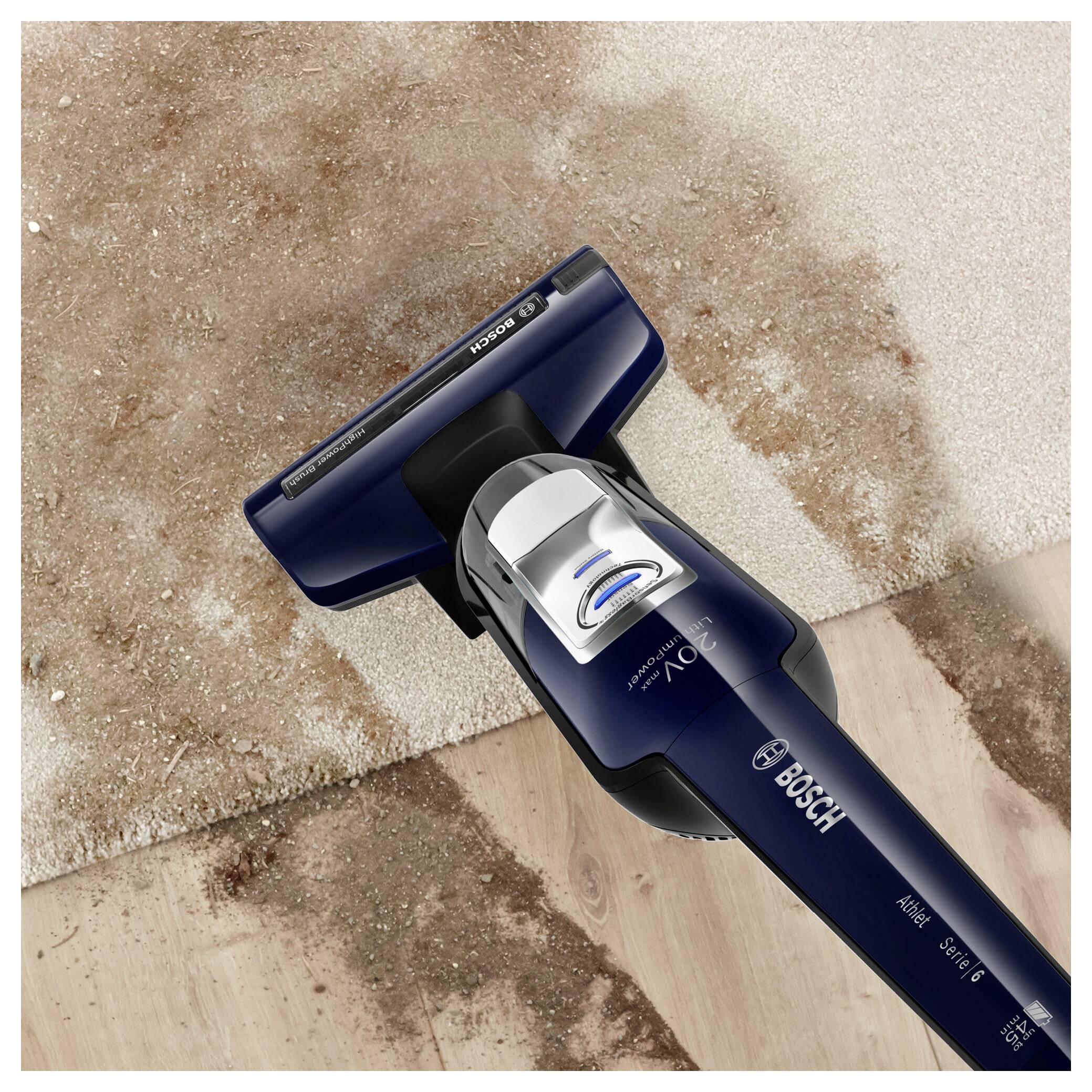 Un aspirateur se déplace sur un tapis, éliminant efficacement la saleté et les débris. L'appareil se trouve sur un sol en bois à côté du tapis.