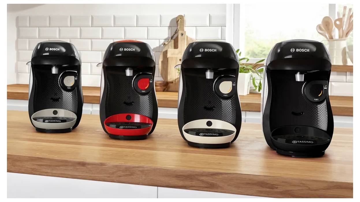 Quatre machines à café noires de Bosch sont alignées sur un comptoir en bois dans un décor de cuisine avec un carrelage blanc en crédence.