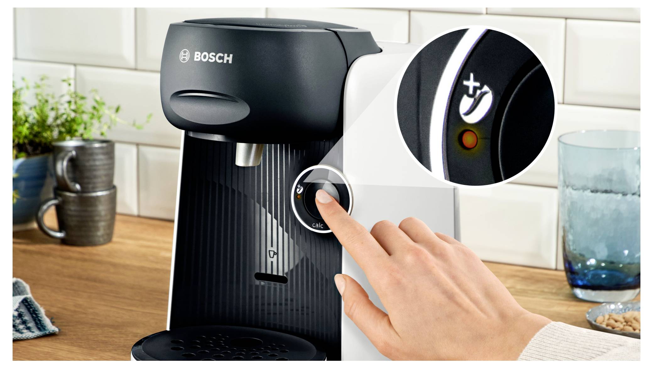 Une main appuie sur un bouton d'une machine à café Bosch avec un gros plan sur l'icône de mise en marche, indiquant une fonctionnalité de l'appareil.