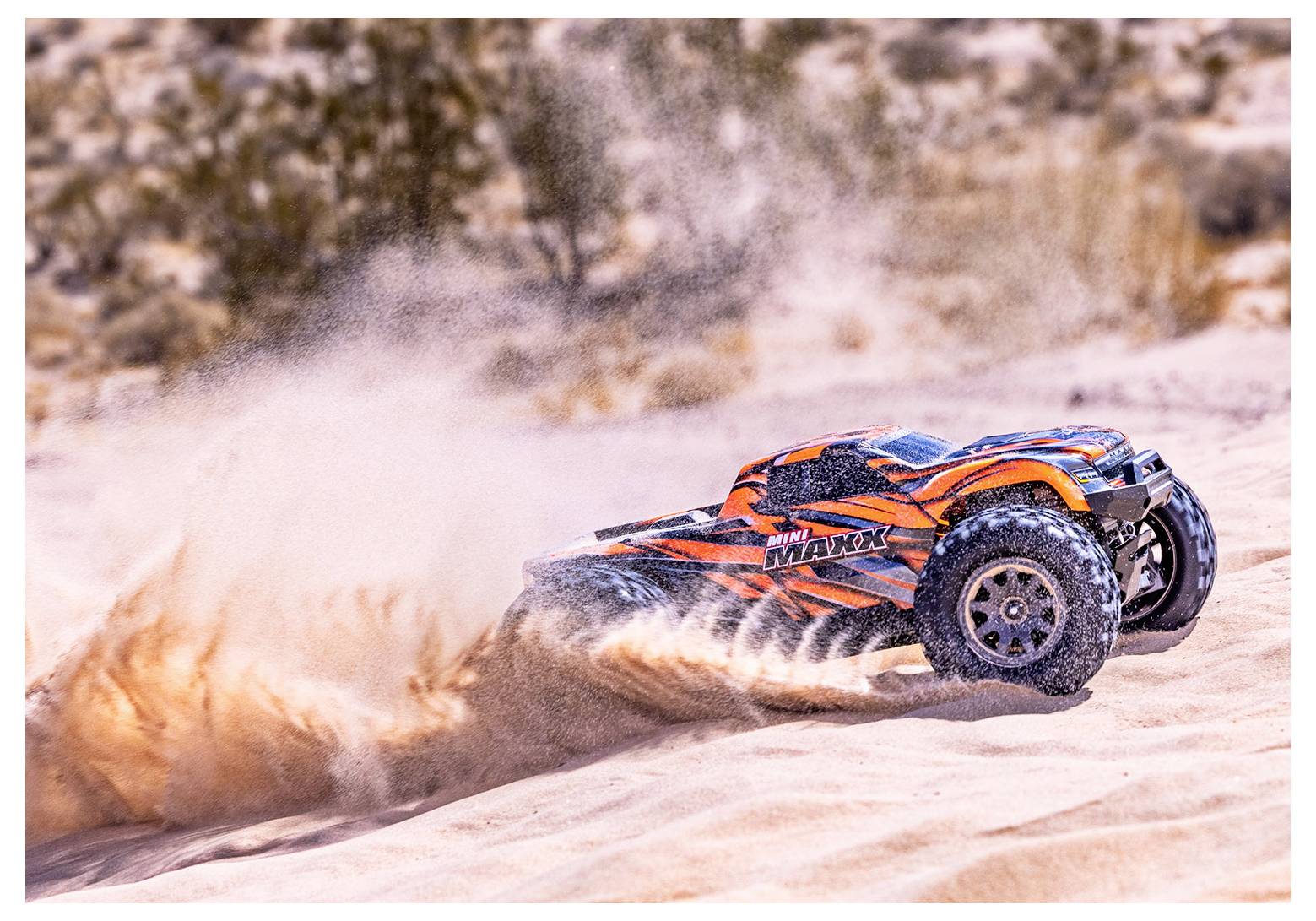 Une voiture télécommandée orange et bleue file à travers un terrain sablonneux, soulevant de la poussière derrière elle dans un décor désertique.