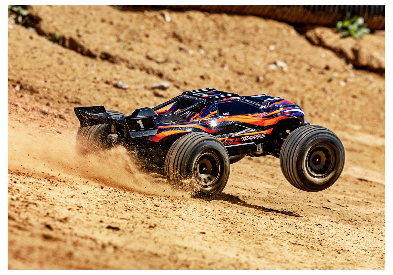 Une voiture télécommandée avec des flammes et des rayures sur la carrosserie file sur une piste de terre, soulevant un nuage de poussière.