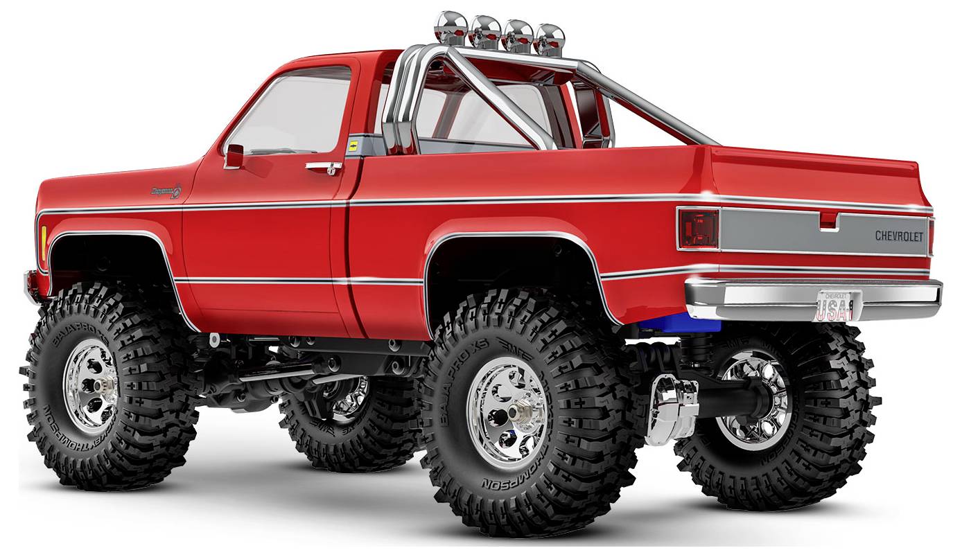Un camion tout-terrain rouge avec de grandes roues et des détails chromés, stationné sur un fond blanc, mettant en valeur son design robuste et ses modifications.