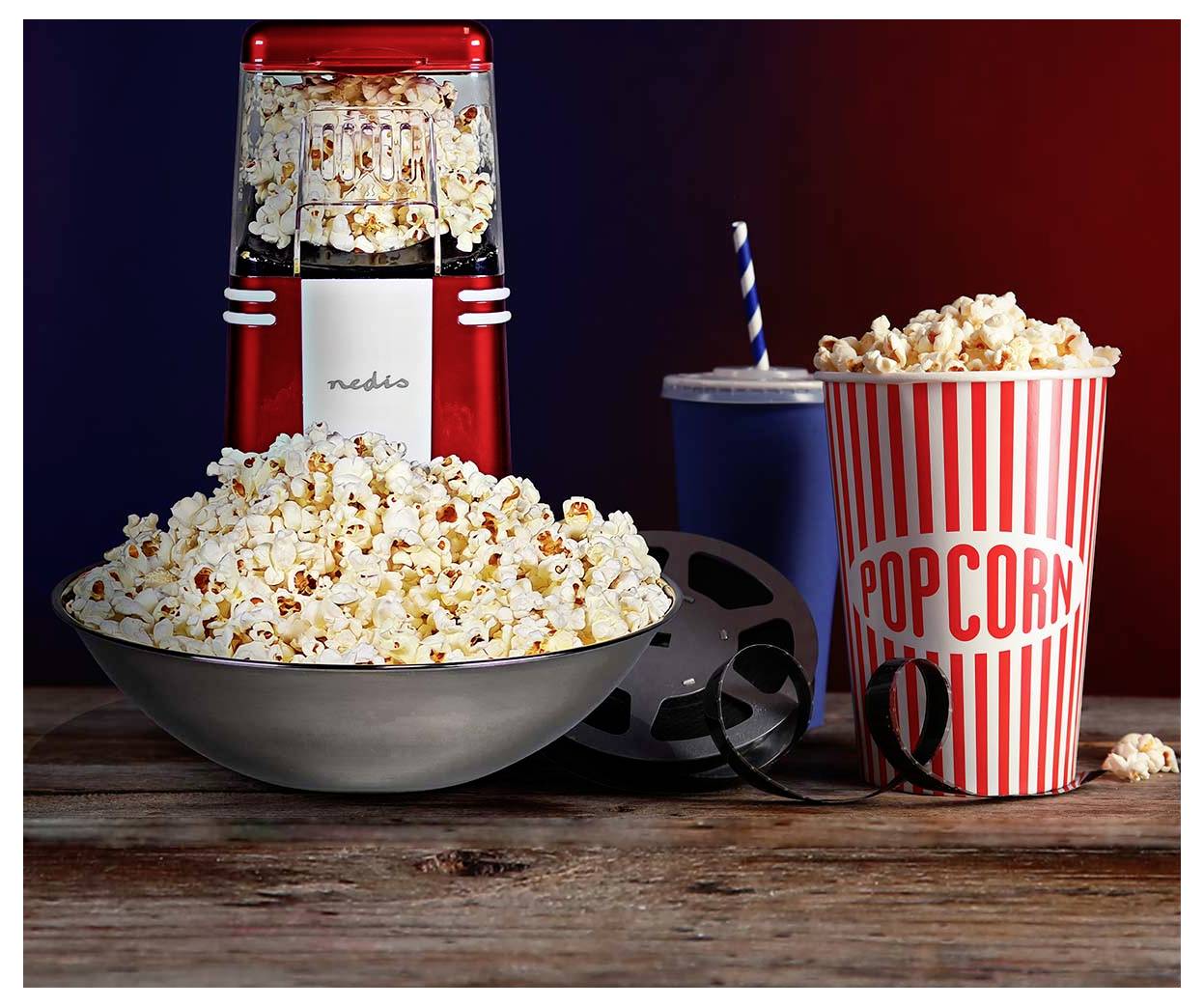 'Machine à pop-corn à côté d'un bol et d'un gobelet rayé rempli de pop-corn, avec un rouleau de film et une boisson avec une paille, sur une table en bois.'