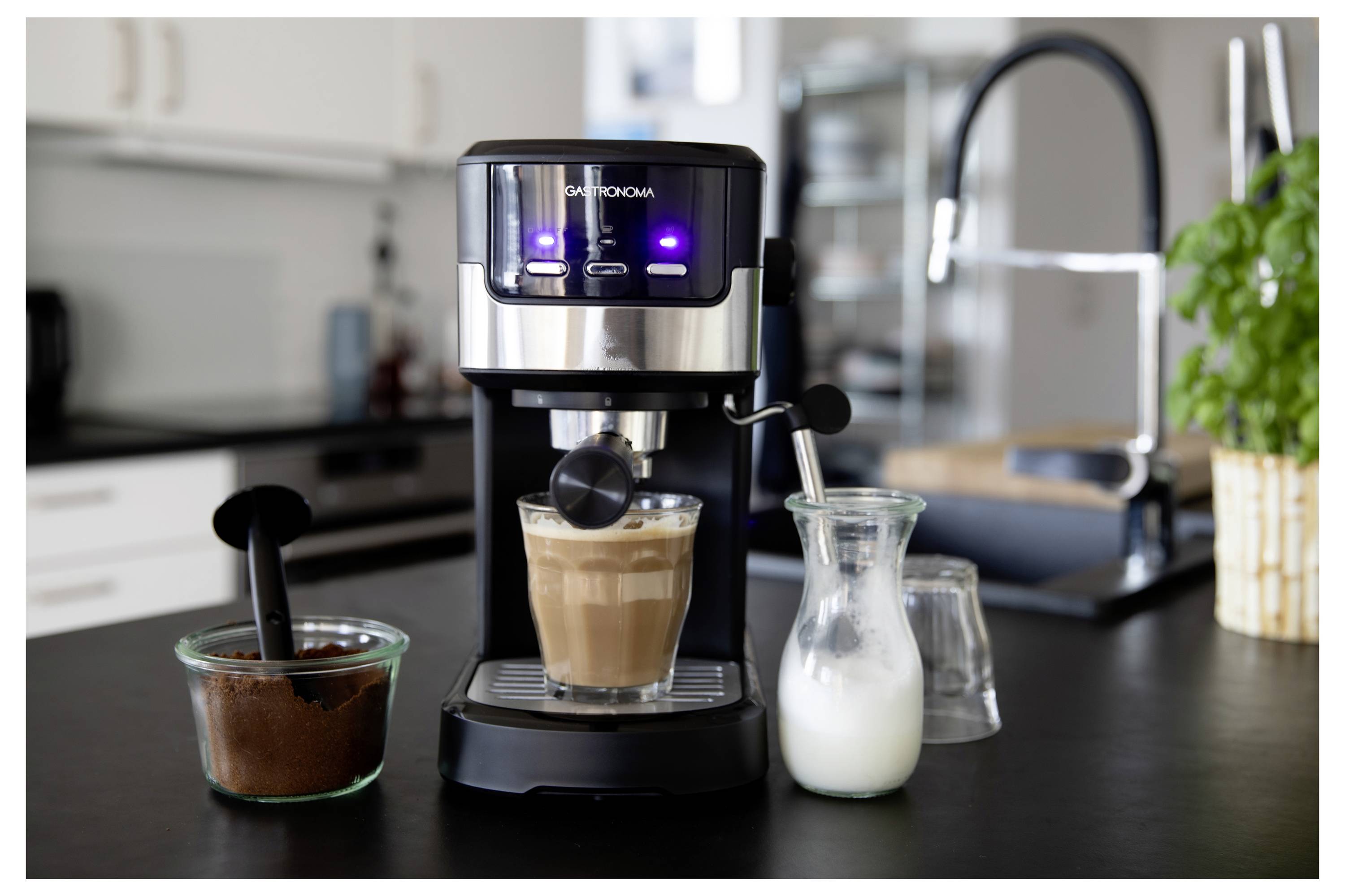 Machine à espresso sur un comptoir de cuisine avec une tasse de café, un pot de lait mousseux et un bol de café moulu à côté.