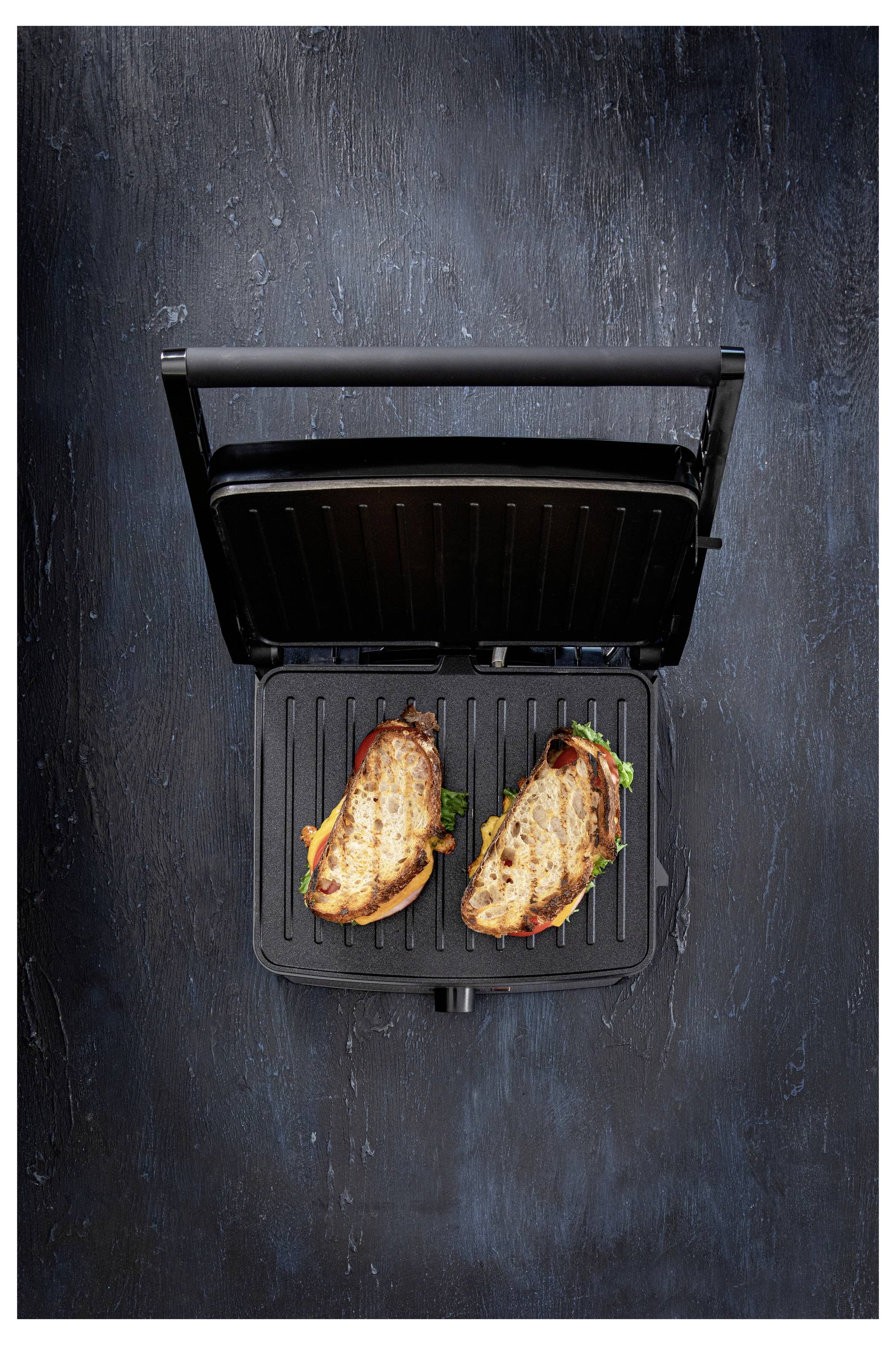 Deux sandwichs grillés au fromage fondu et à la laitue, préparés sur un grill panini, vus de dessus, sur une surface sombre texturée.