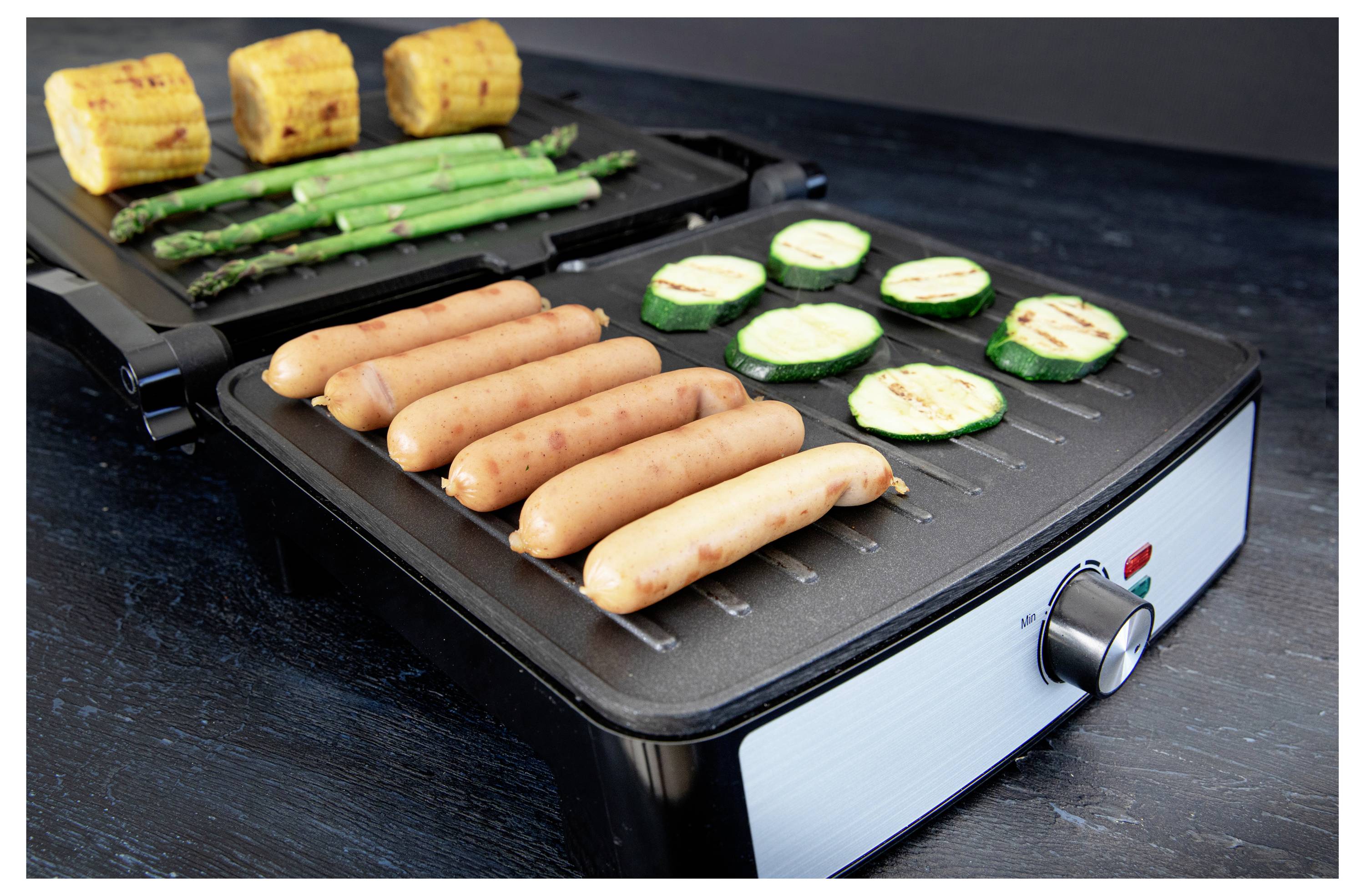 Un grill électrique avec des saucisses, du maïs, des asperges et des tranches de courgettes, présentant une variété de légumes et de viandes en train d'être grillés.