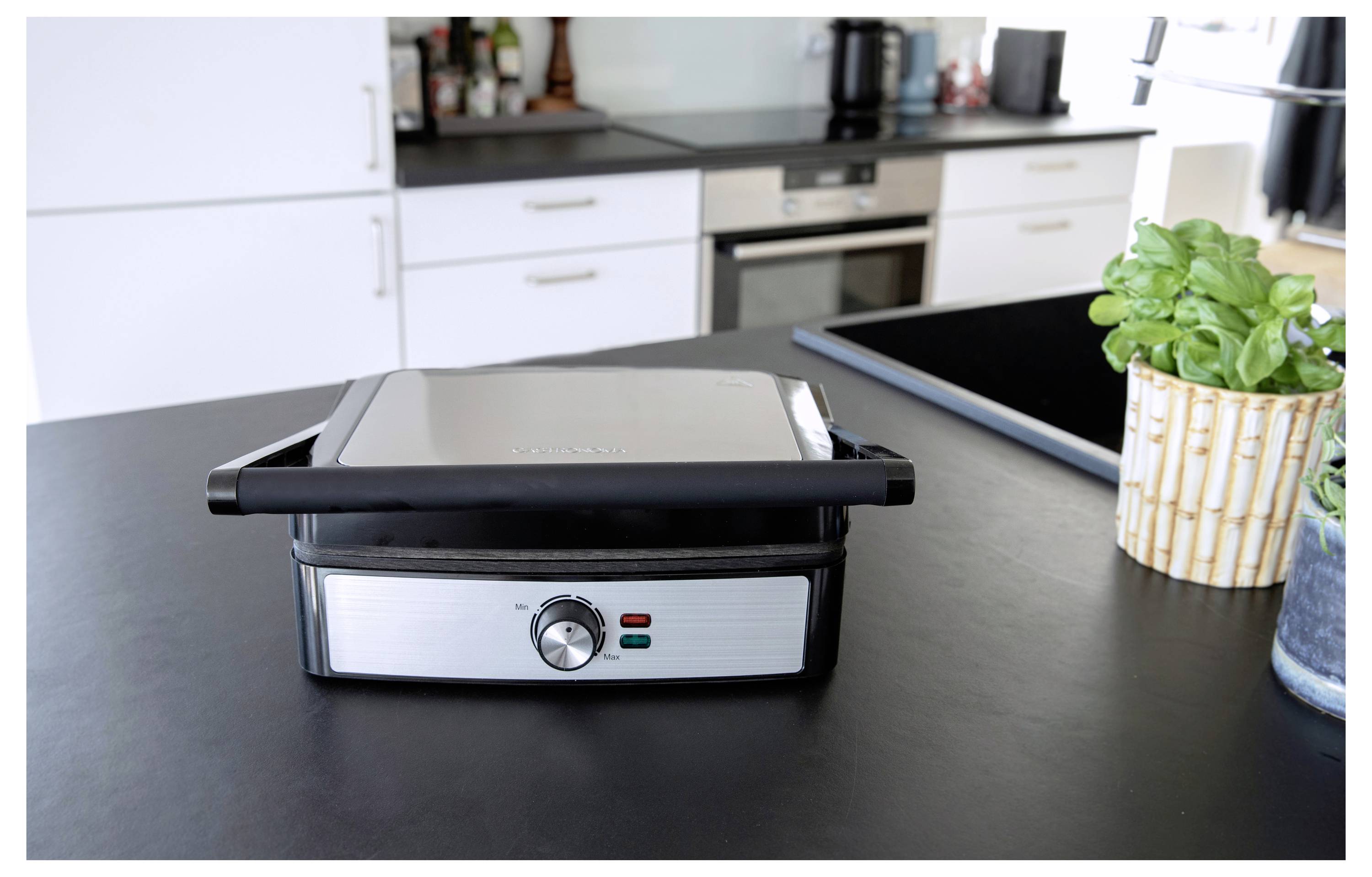 Un plan de travail de cuisine avec un grill électrique fermé au premier plan. Le grill est équipé d'un cadran de température et de voyants lumineux.