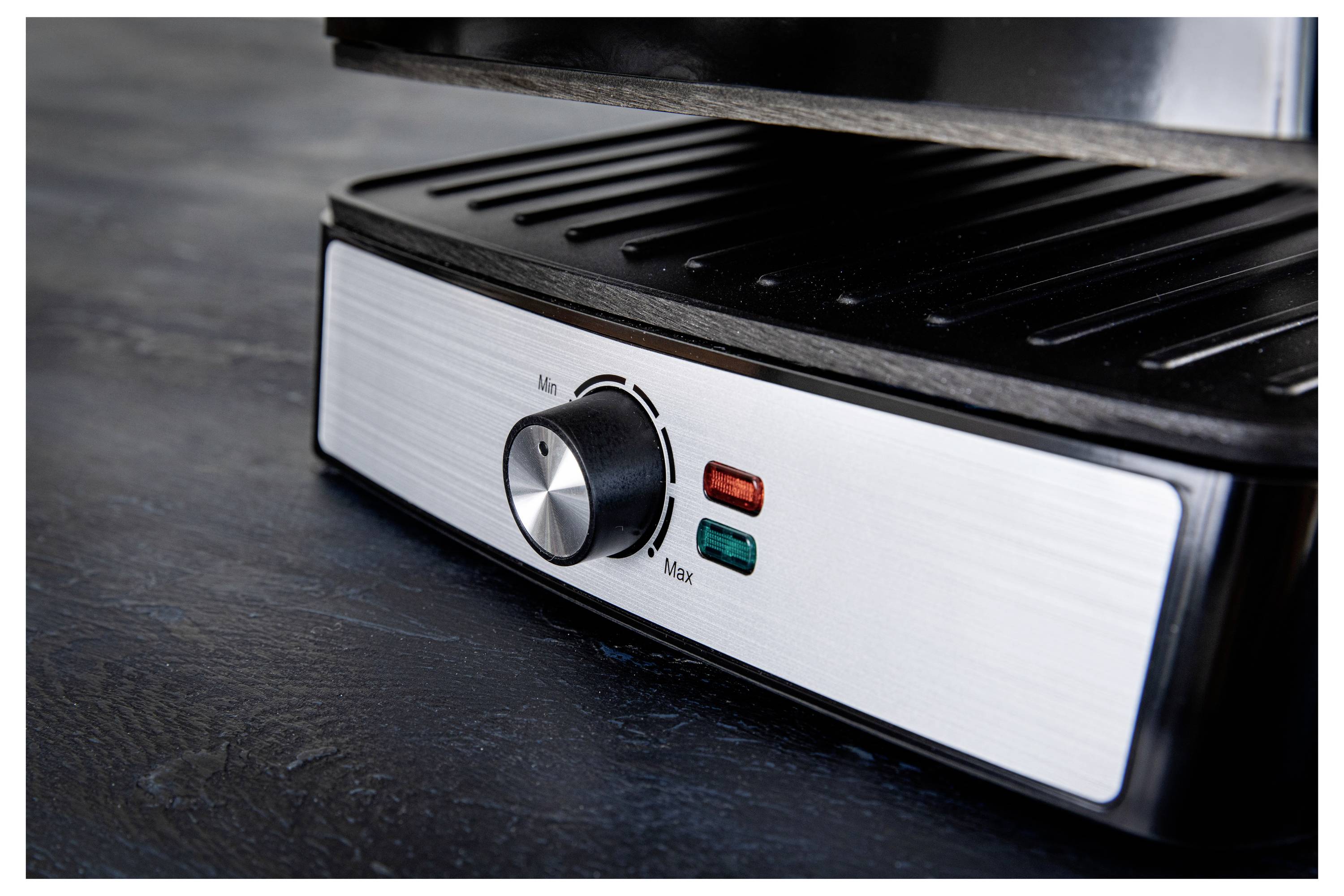 Une presse à panini en acier inoxydable avec un cadran de température et deux voyants lumineux. La surface présente des rainures de grill pour la cuisson.