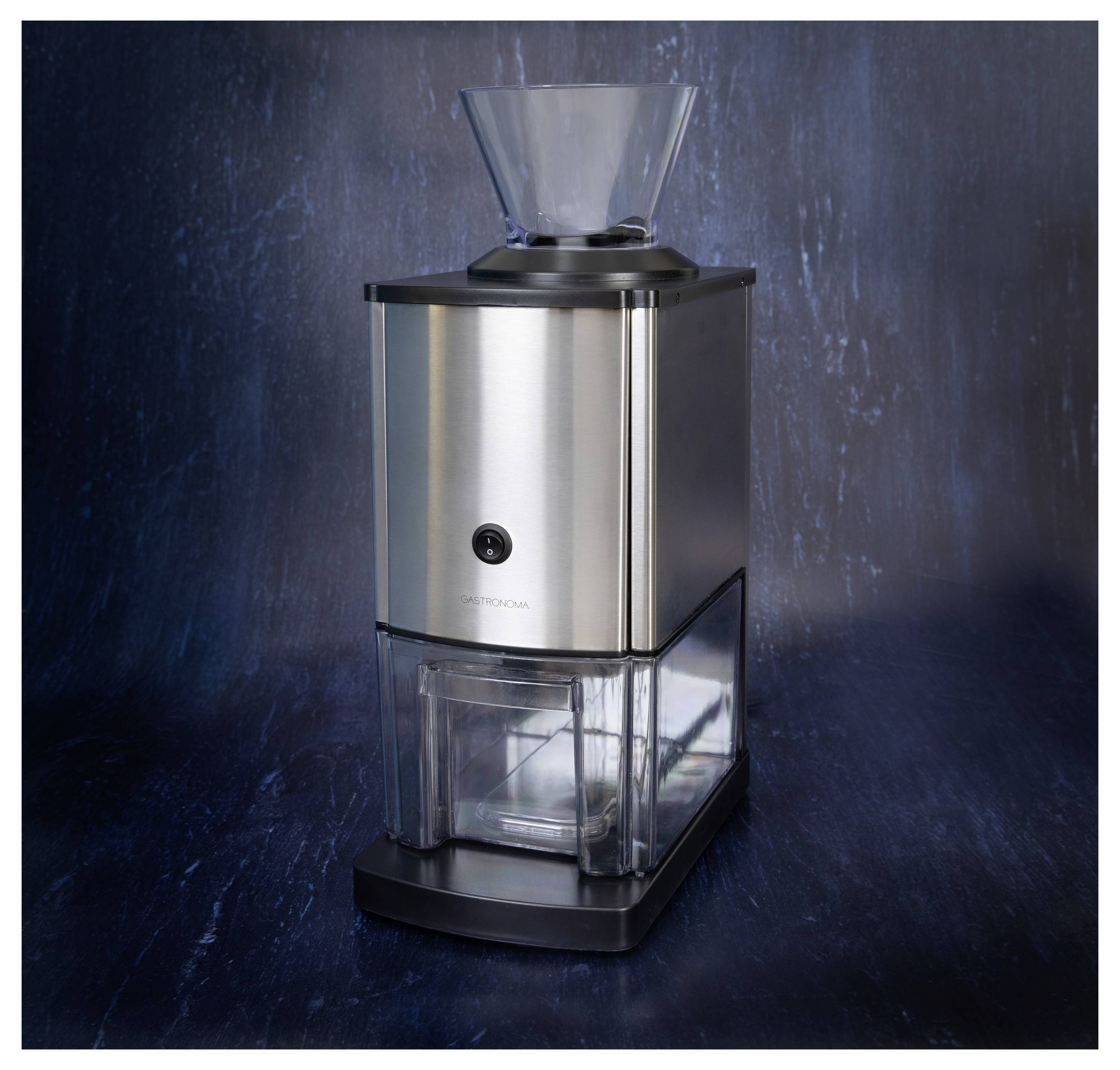 Un broyeur électrique en acier inoxydable doté d'un réservoir à grains transparent en plastique placé sur le dessus, posé contre un fond texturé bleu marine.