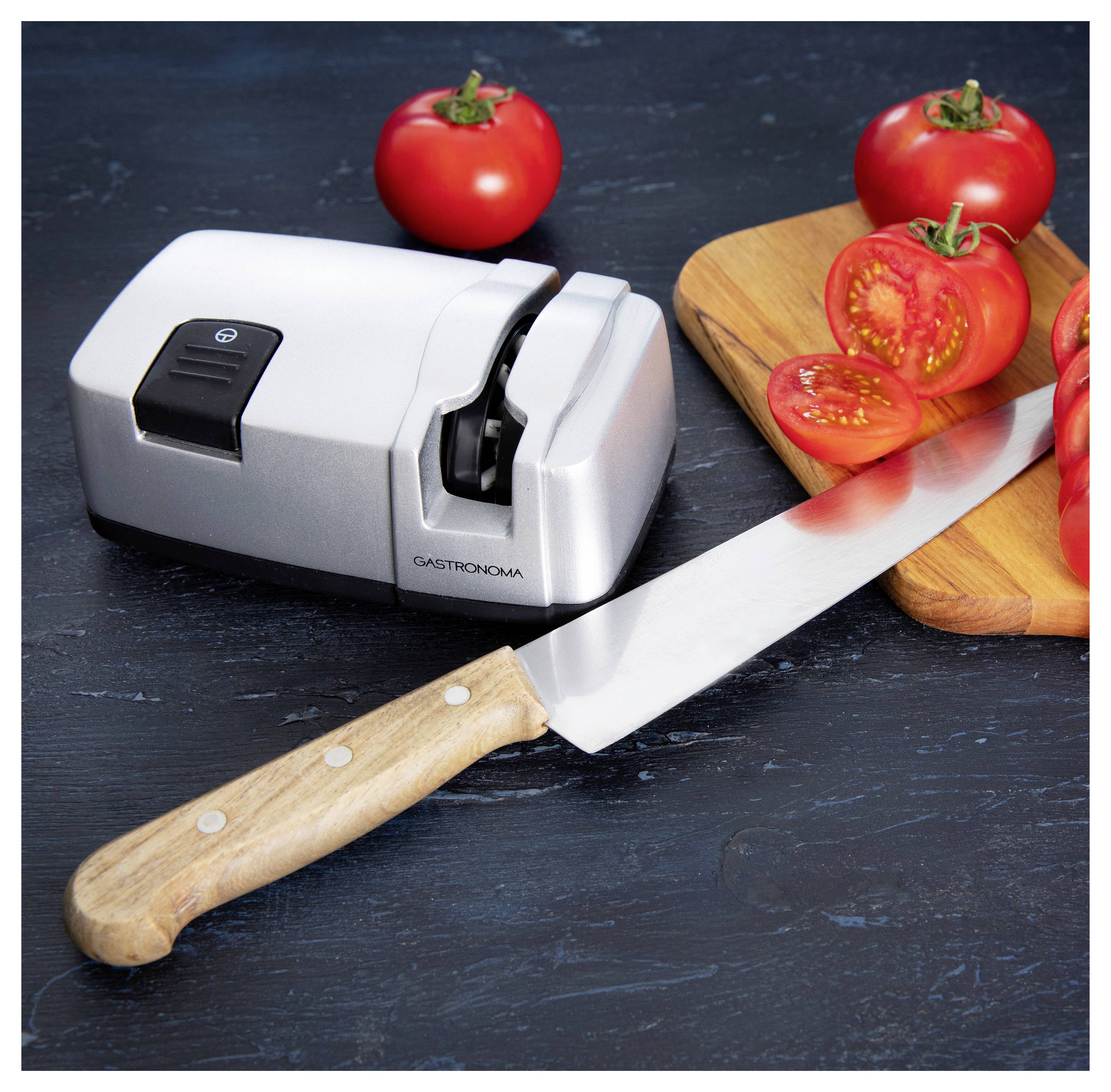 Un couteau de cuisine avec un manche en bois est placé à côté d'un aiguiseur de couteaux en argent et de tomates tranchées sur une planche à découper.