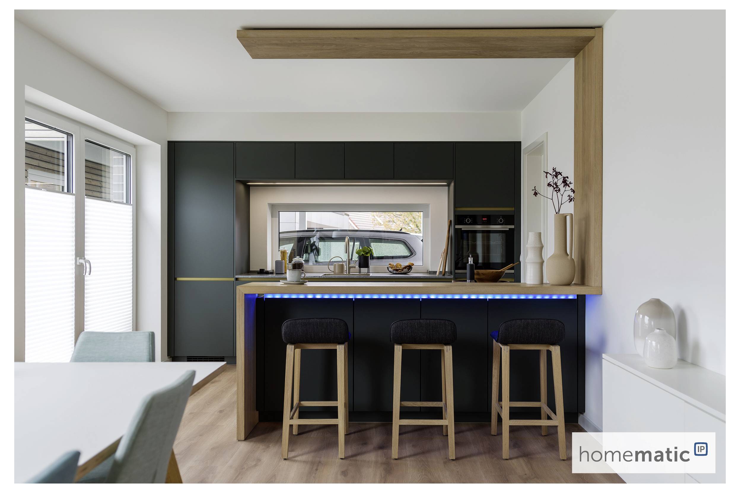 Cuisine moderne avec un îlot central à comptoir noir, quatre tabourets, un éclairage d'ambiance bleu, et vue sur une voiture garée à l'extérieur par une fenêtre.