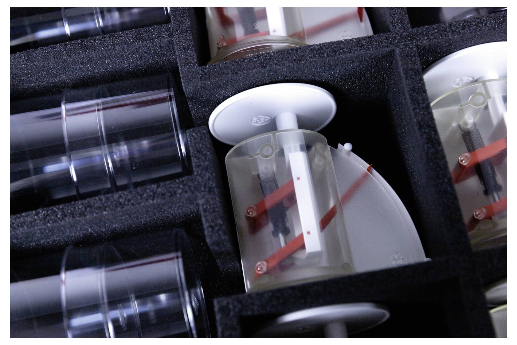 Clear containers with red indicators arranged in foam slots, possibly part of a mechanical or scientific device.