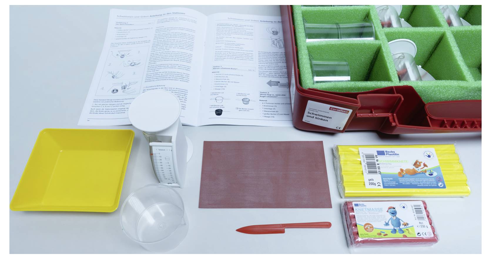 Science experiment kit with a red tray containing test tubes, colored molds, a yellow tray, measuring cup, and instructions booklet.