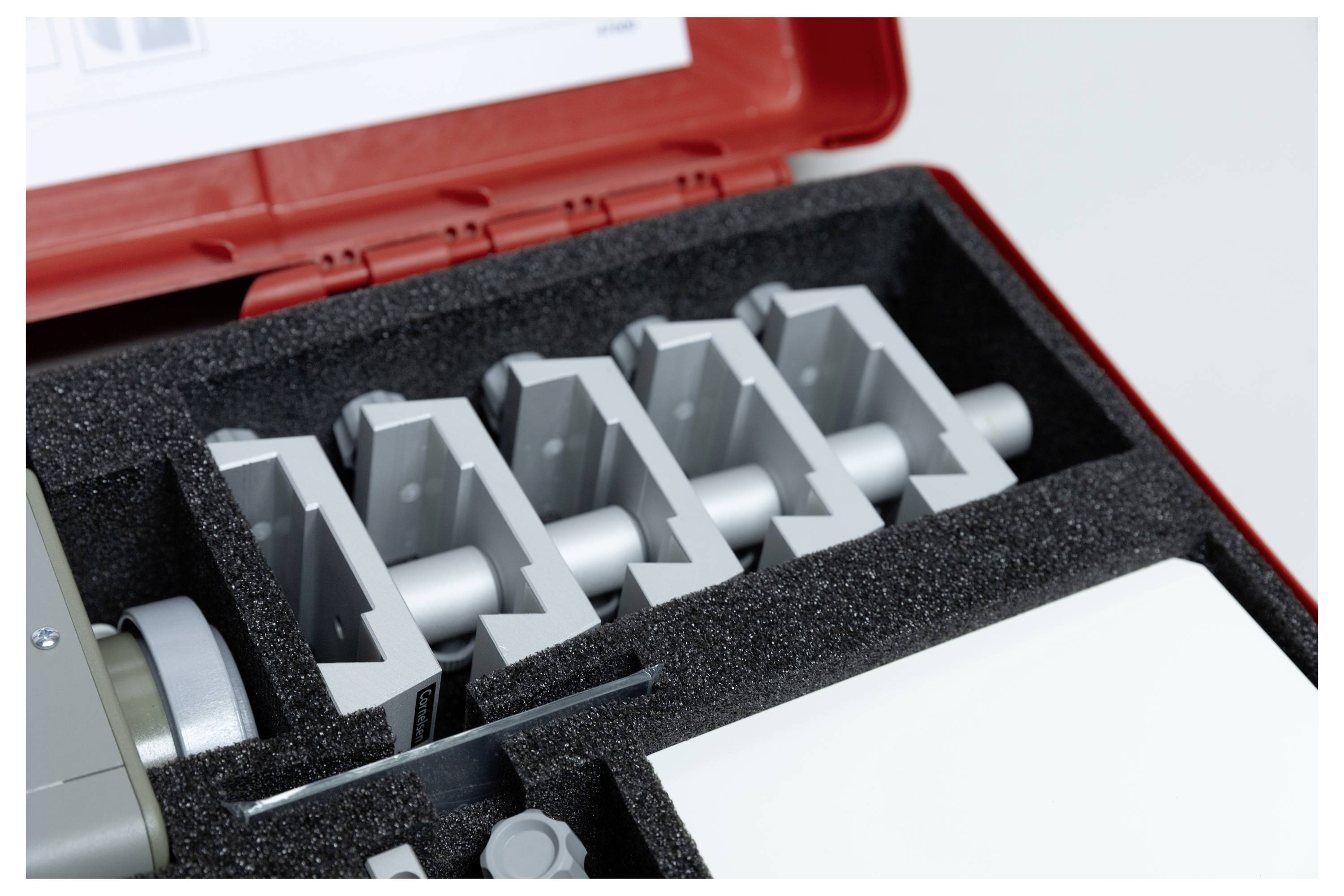 A red case with protective foam holding gray metal blocks arranged in a row. The top of the case has a white label with text.