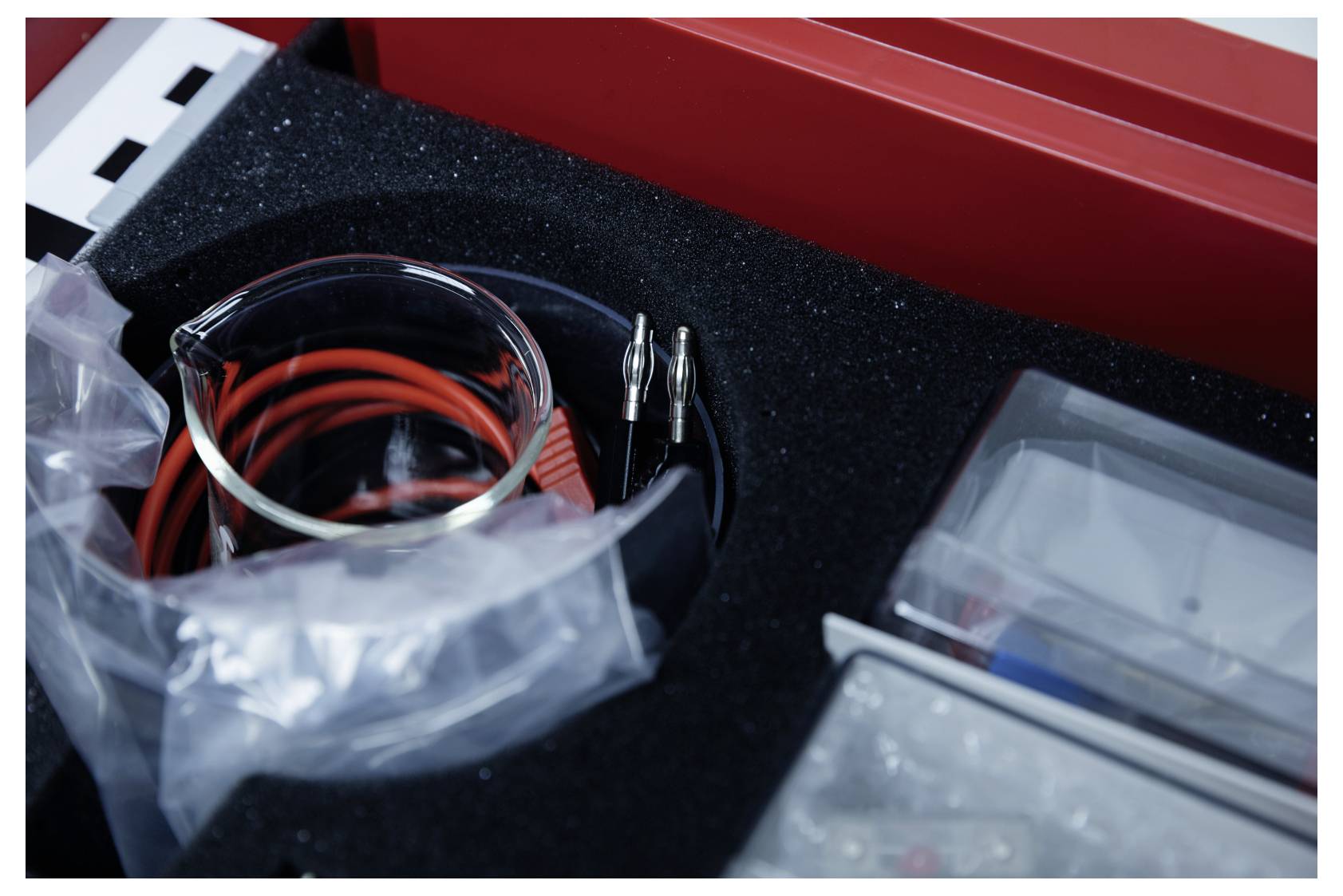 An electrical toolkit with red and black coiled wires, alligator clips, and compartments, suggesting use for technical work or repairs.
