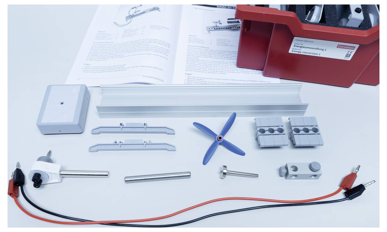 Assorted electrical components, connectors, and a small propeller are arranged on a table with open manuals and a red toolbox in the background.