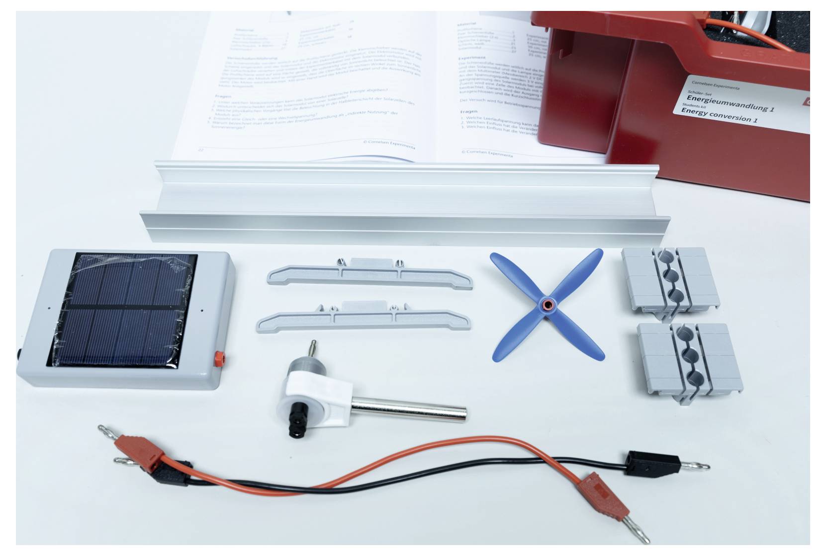 Components for a small solar energy kit including a solar panel, wires, gears, and instruction manual, laid out on a table.