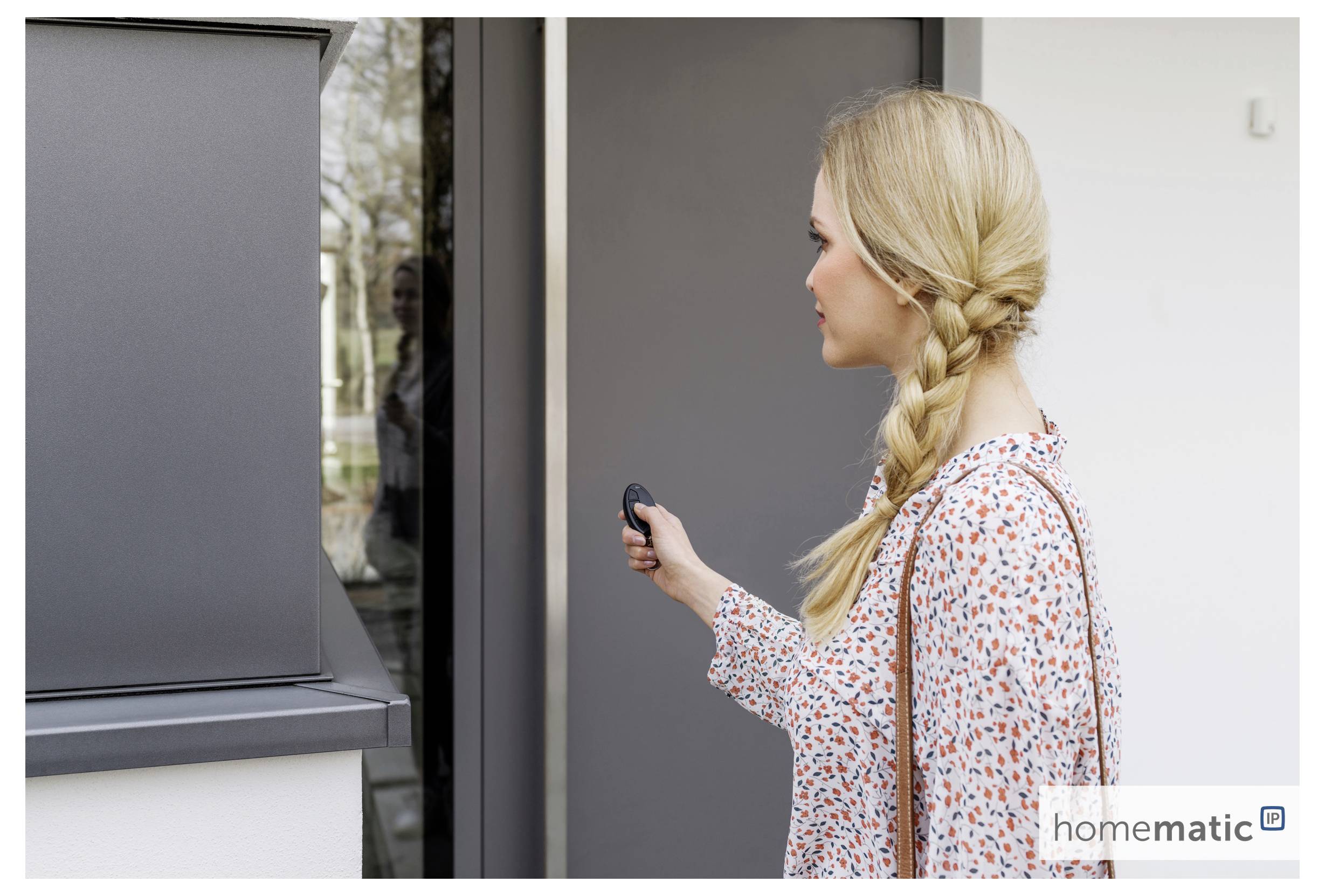 Une personne aux cheveux tressés utilise une télécommande pour déverrouiller ou interagir avec une porte au design moderne.