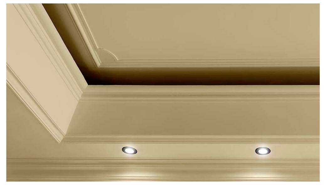 Un plafond beige avec des moulures décoratives et deux lumières encastrées illuminant une pièce.