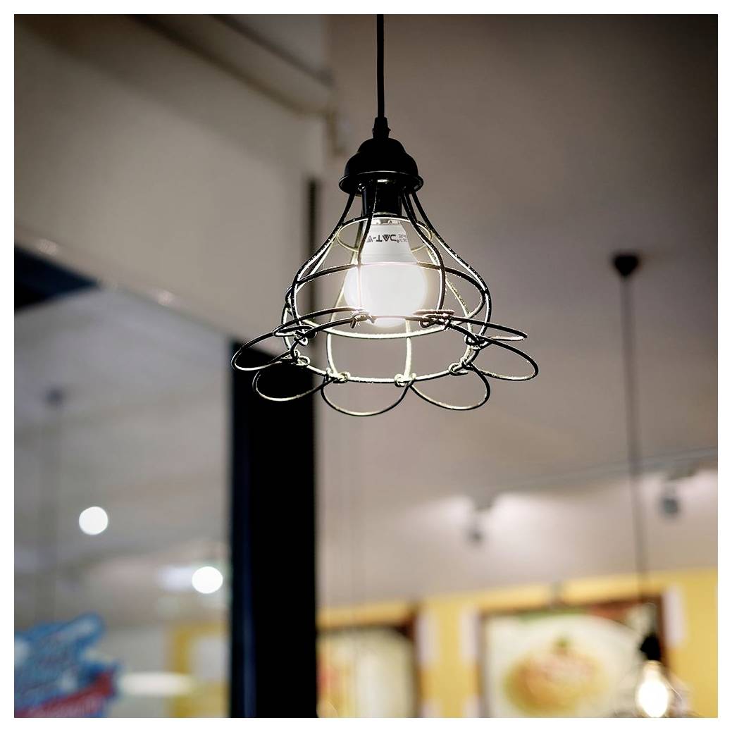 Une ampoule suspendue avec un abat-jour en grille métallique est allumée, placée dans un intérieur doucement éclairé avec des détails de fond floutés.