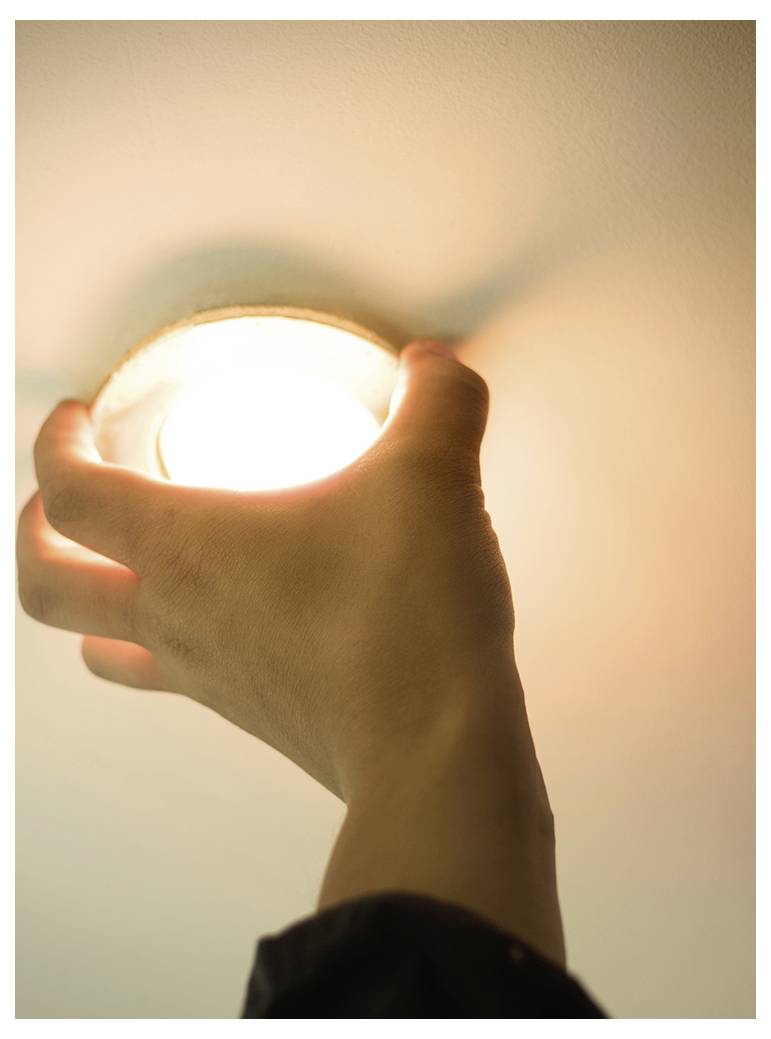Une main installe une ampoule ronde de plafonnier, créant une lueur douce sur le plafond.