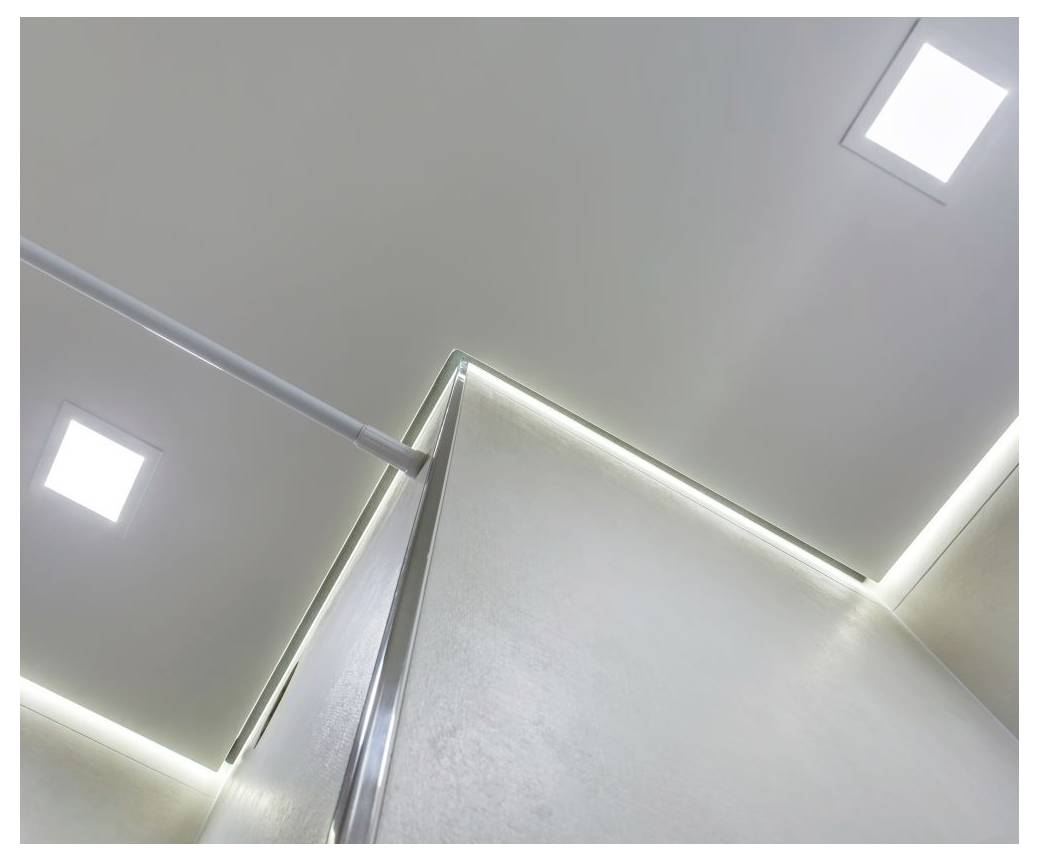 Vue d'un plafond de chambre moderne et minimaliste avec un éclairage encastré et des bandes LED soulignant les bords, créant une ambiance épurée.