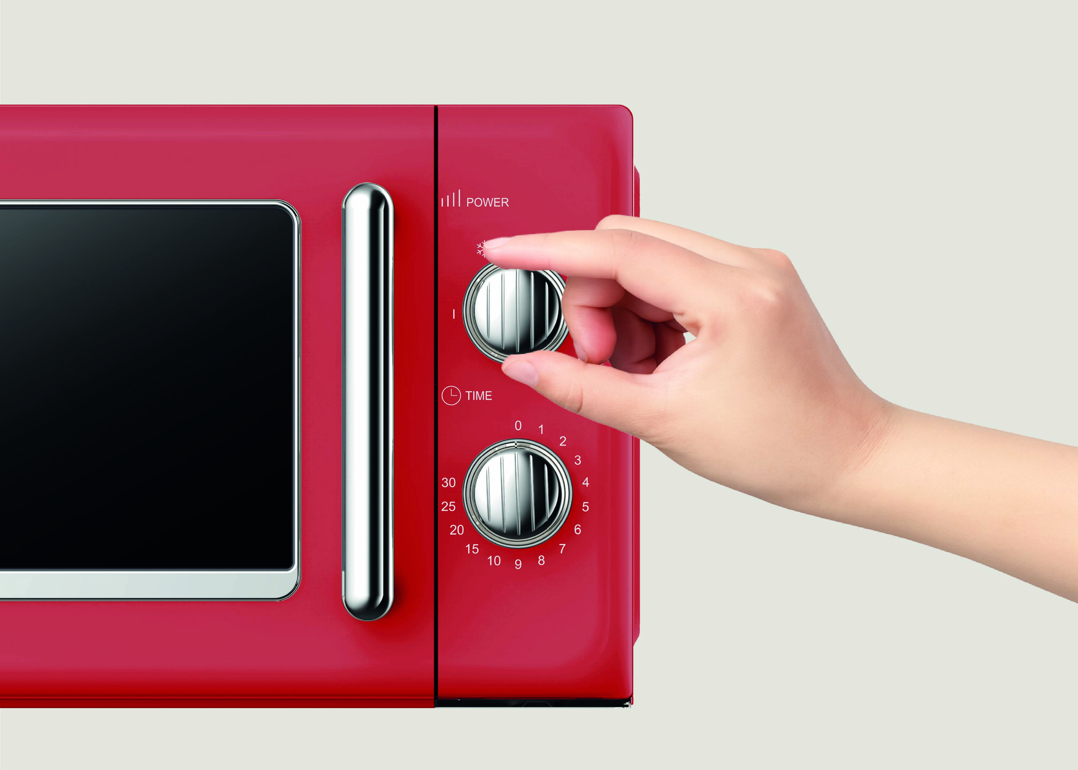 Une main ajuste le cadran du minuteur sur un four à micro-ondes rouge, avec le réglage de puissance visible à proximité.
