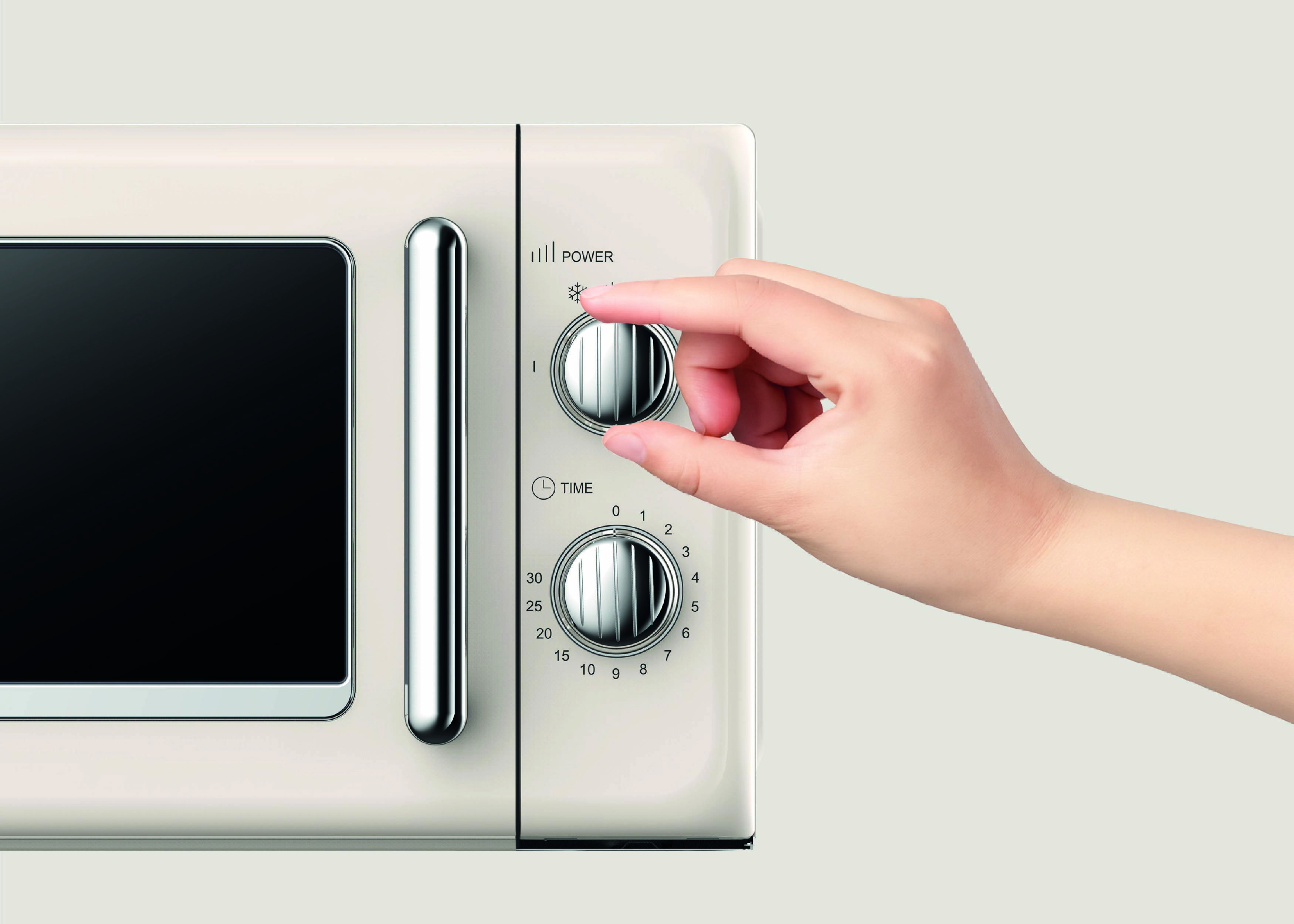 Un doigt ajuste le bouton de réglage de puissance sur un four à micro-ondes, indiquant le fonctionnement d'un appareil de cuisine pour la cuisson ou le réchauffage des aliments.