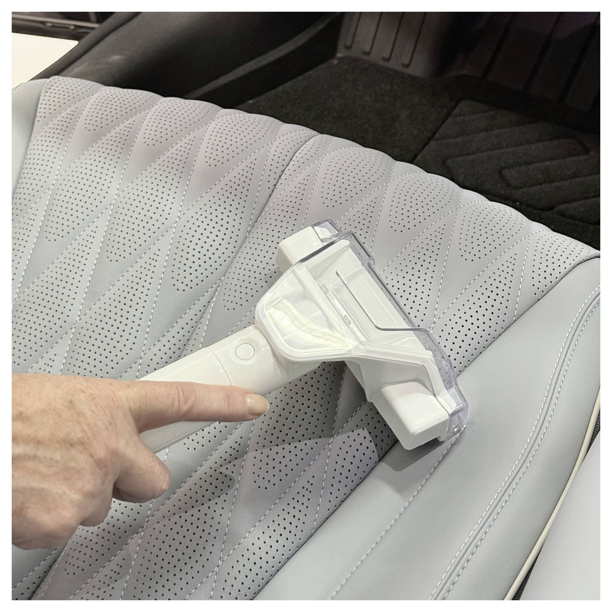 Une personne démontre l'utilisation d'un aspirateur portable sur un siège de voiture, illustrant son efficacité à éliminer les saletés des garnitures.