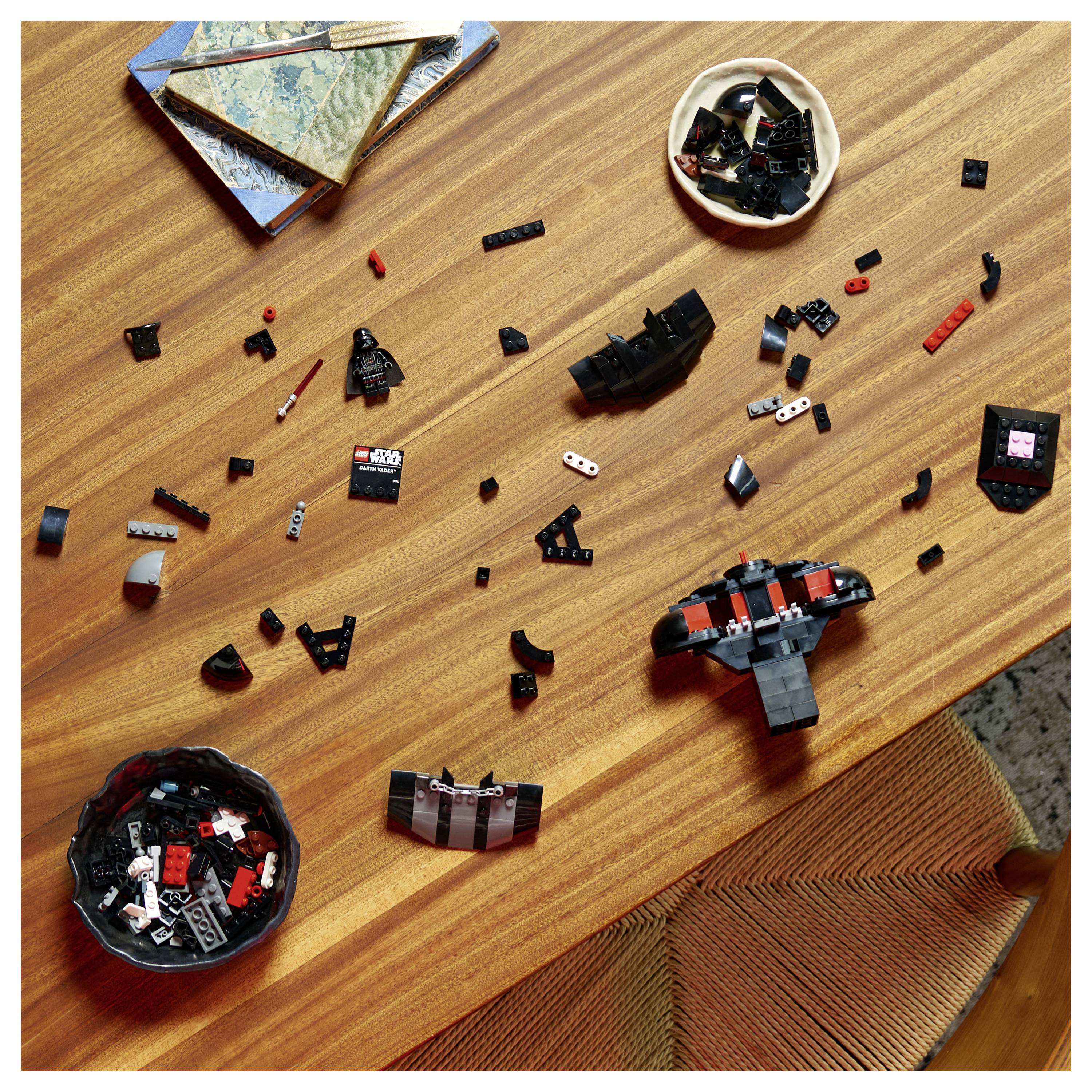 Des pièces de Lego éparpillées sur une table en bois avec des livres et un bol rond à proximité, suggérant une activité de construction en cours.