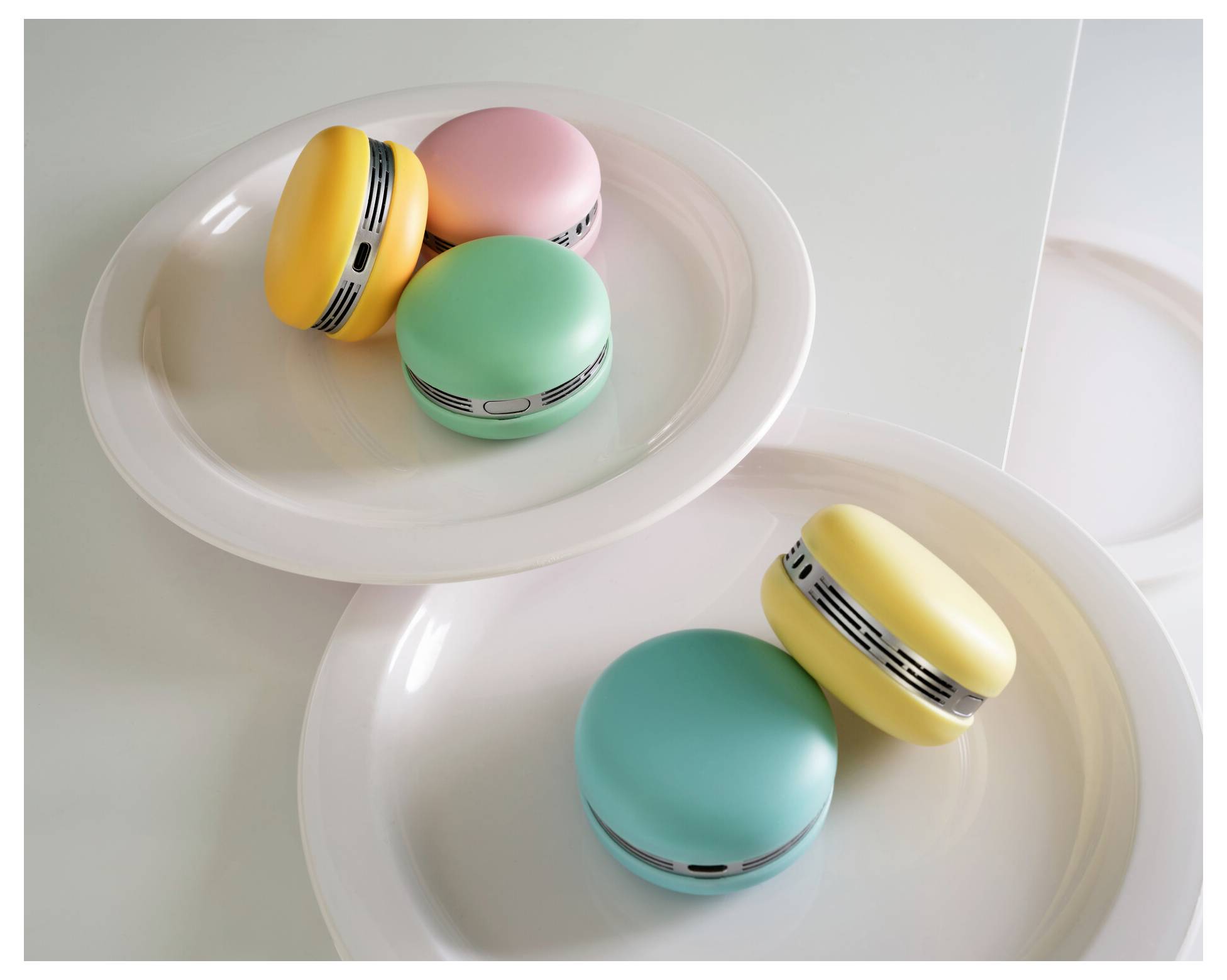 Trois objets colorés en forme de macaron posés sur des assiettes, ressemblant à des ventilateurs portables alimentés par USB avec des évents.