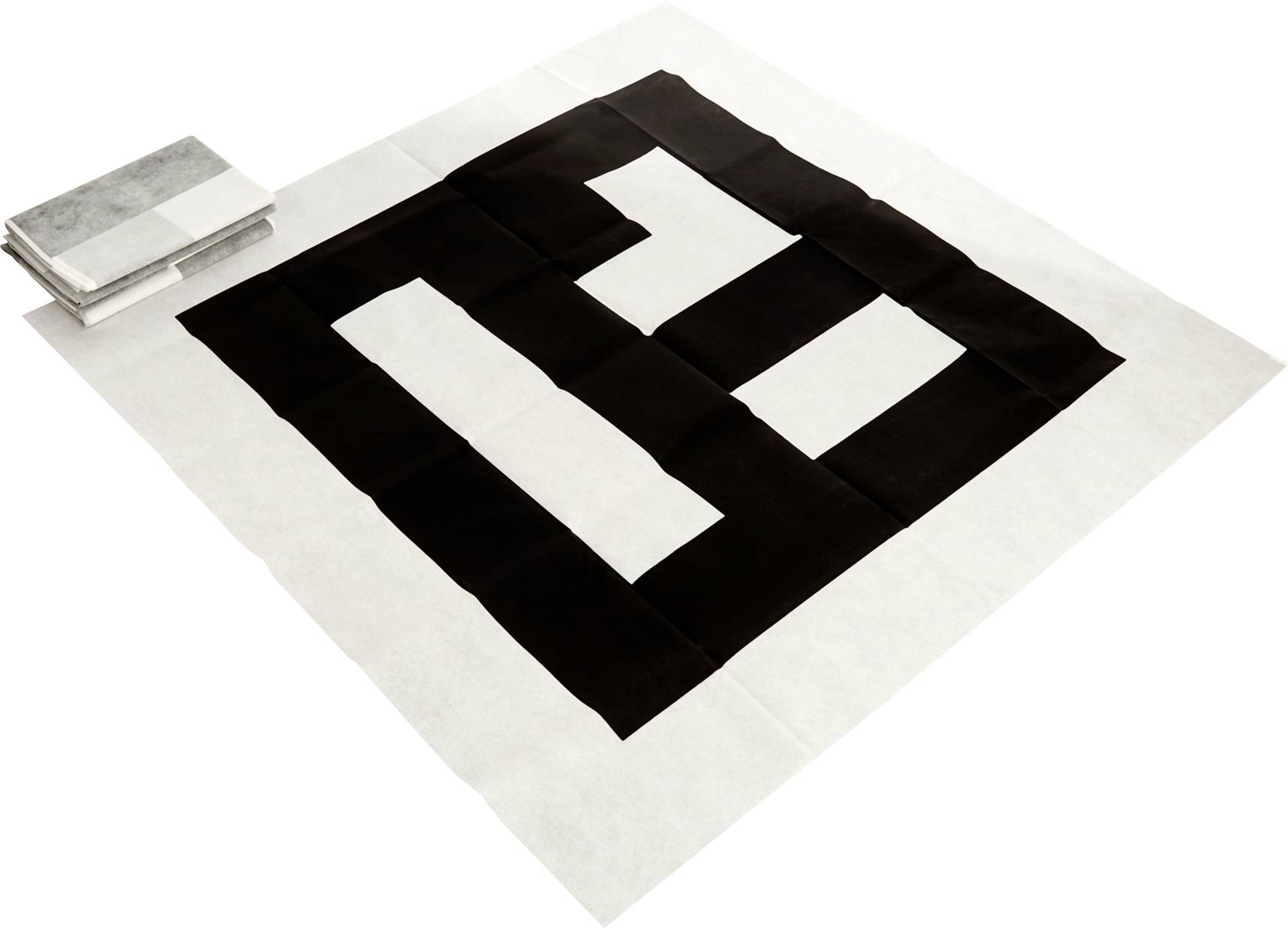 Une grande œuvre d'art textile présente un motif géométrique audacieux en carrés noirs et blancs sur un fond blanc, avec une pile pliée de textiles similaires à côté.